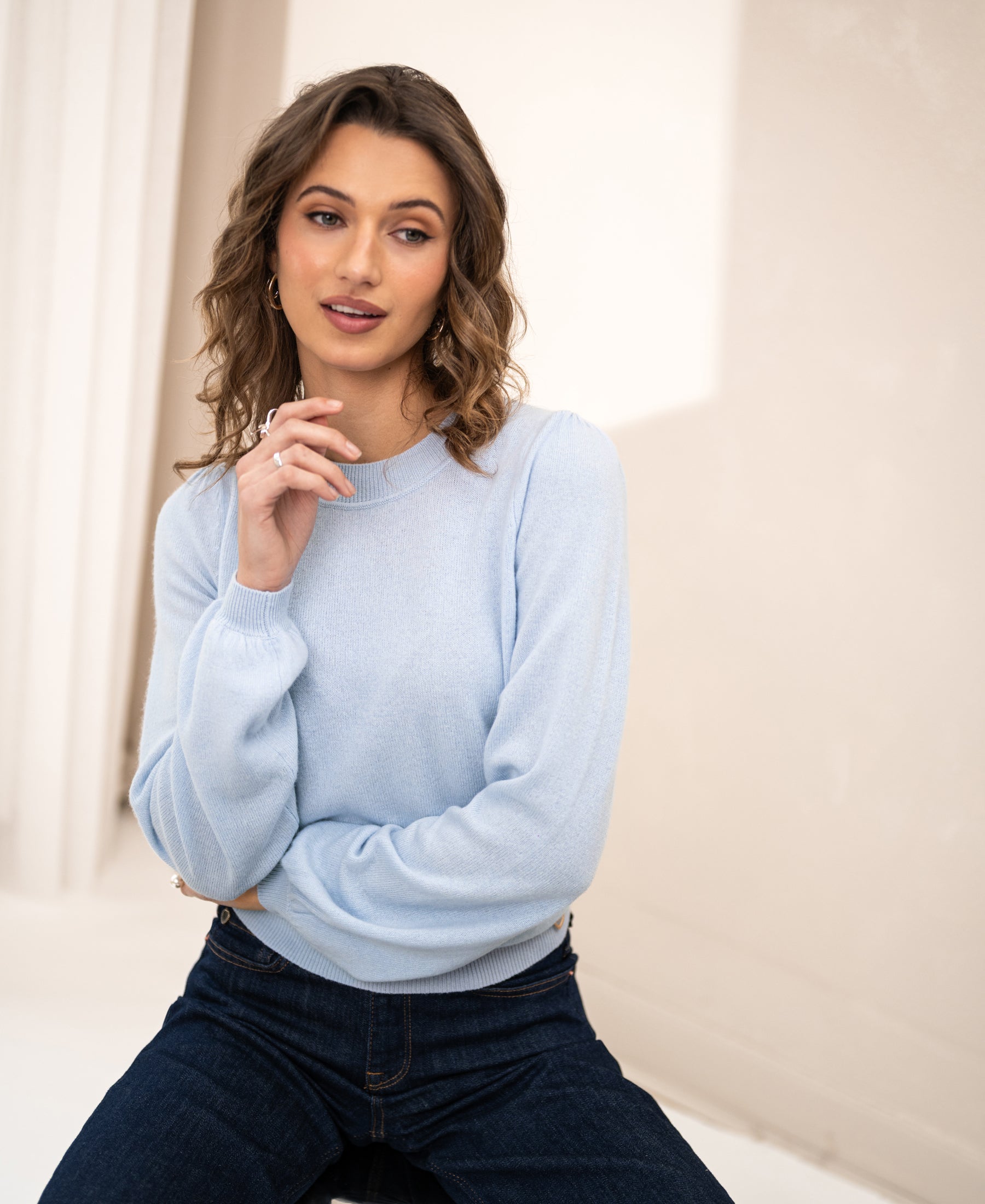 Light blue Plein Publique soft merino wool sweater LA BAYONNE seen indoors, with a woman smiling and hand near her face.