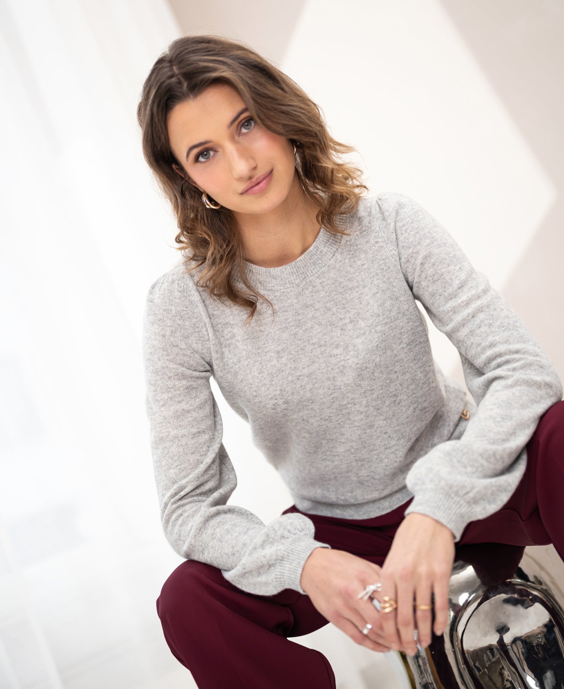 Light grey melange merino wool sweater, shown on a woman with wavy brown hair, front view.