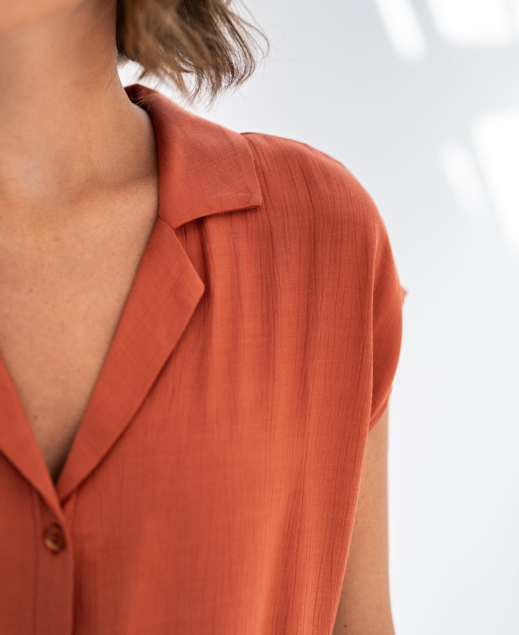 Close-up of a rust sleeveless blouse in soft natural light.
