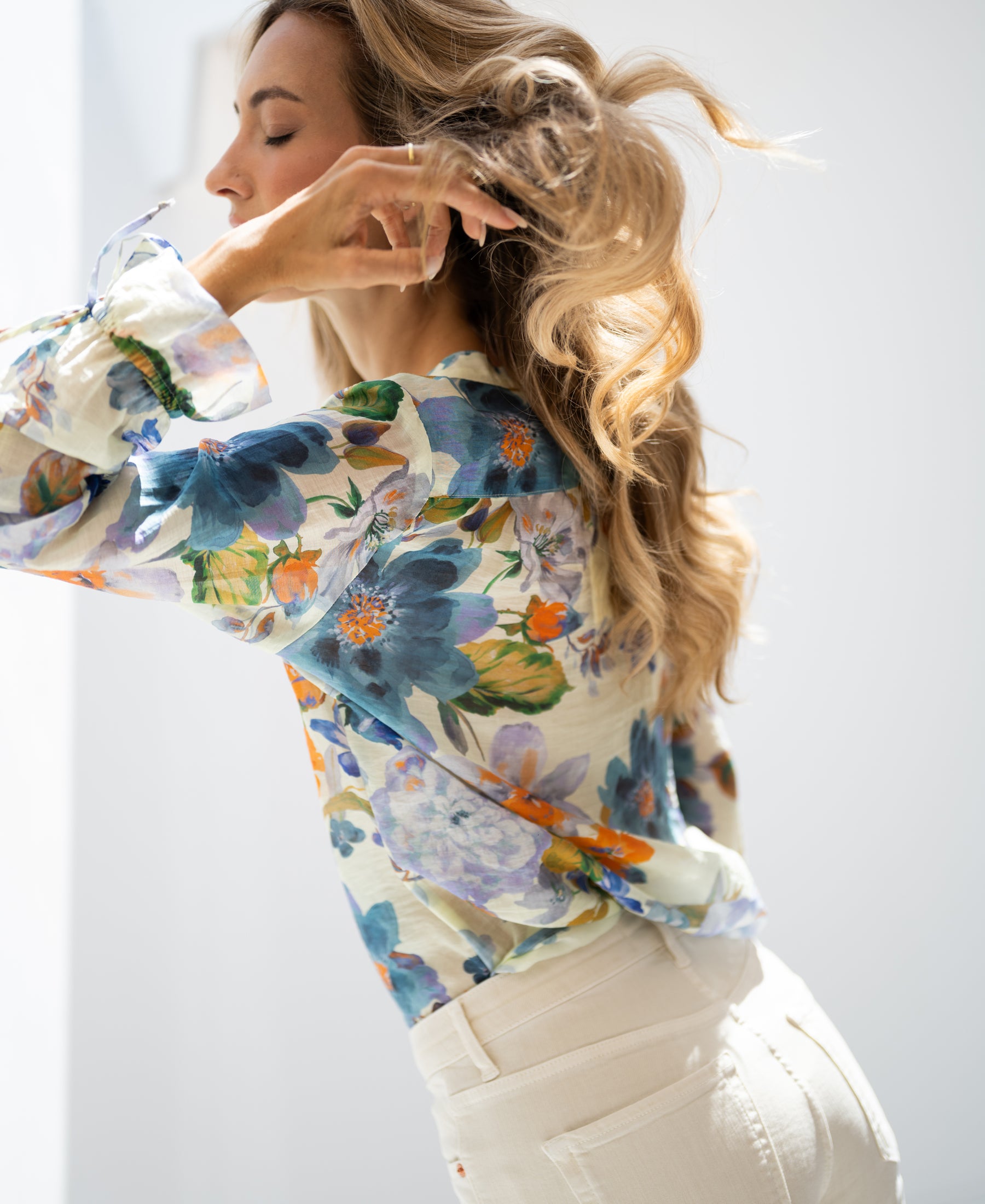 Light blue floral print blouse with wavy-haired model, shown in sunlight.