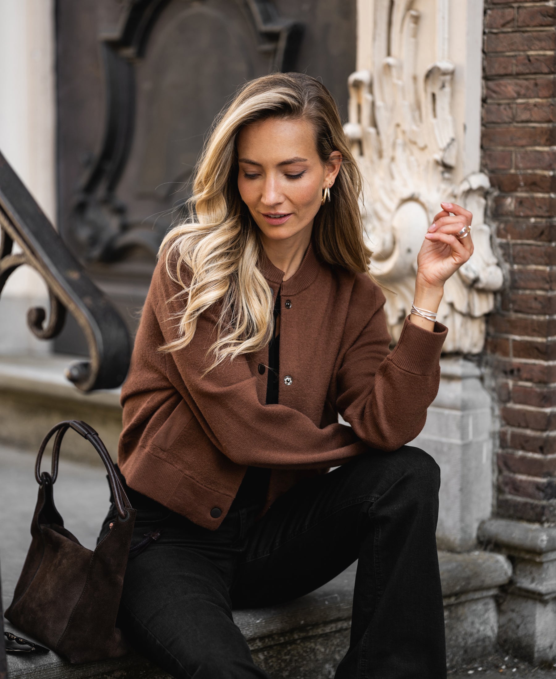 Camel-colored LA BOMBA bomber jacket by PLEIN PUBLIQUE displayed on a model sitting on stone steps.