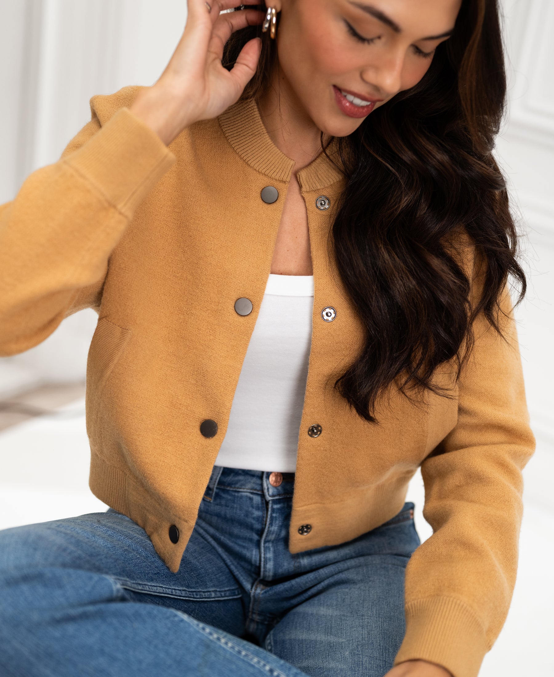 Light camel bomber jacket by PLEIN PUBLIQUE, shown from the front while worn by a woman sitting.