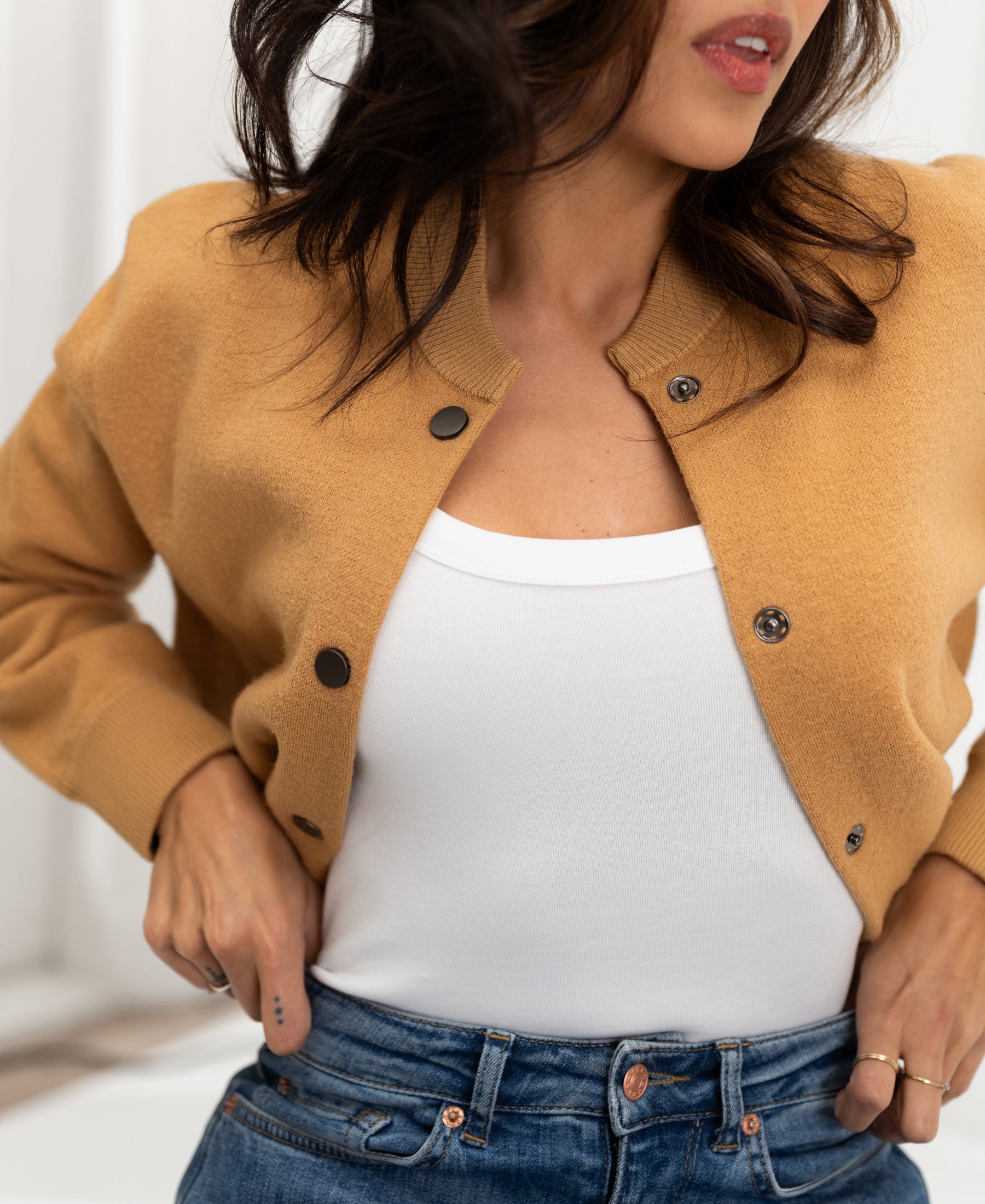 Light camel bomber jacket in a relaxed fit, shown worn by a woman with hands on waist.
