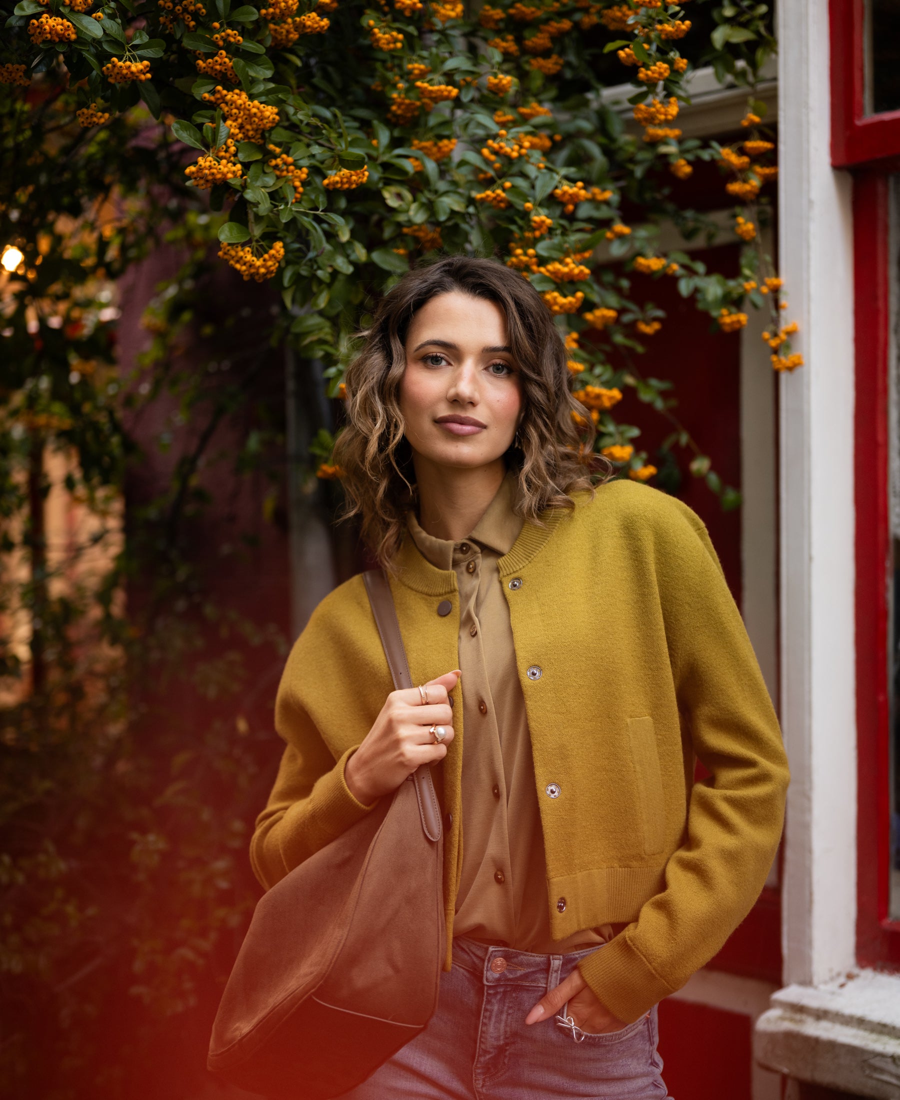 Olive green bomber jacket shown outdoors by orange flowers.