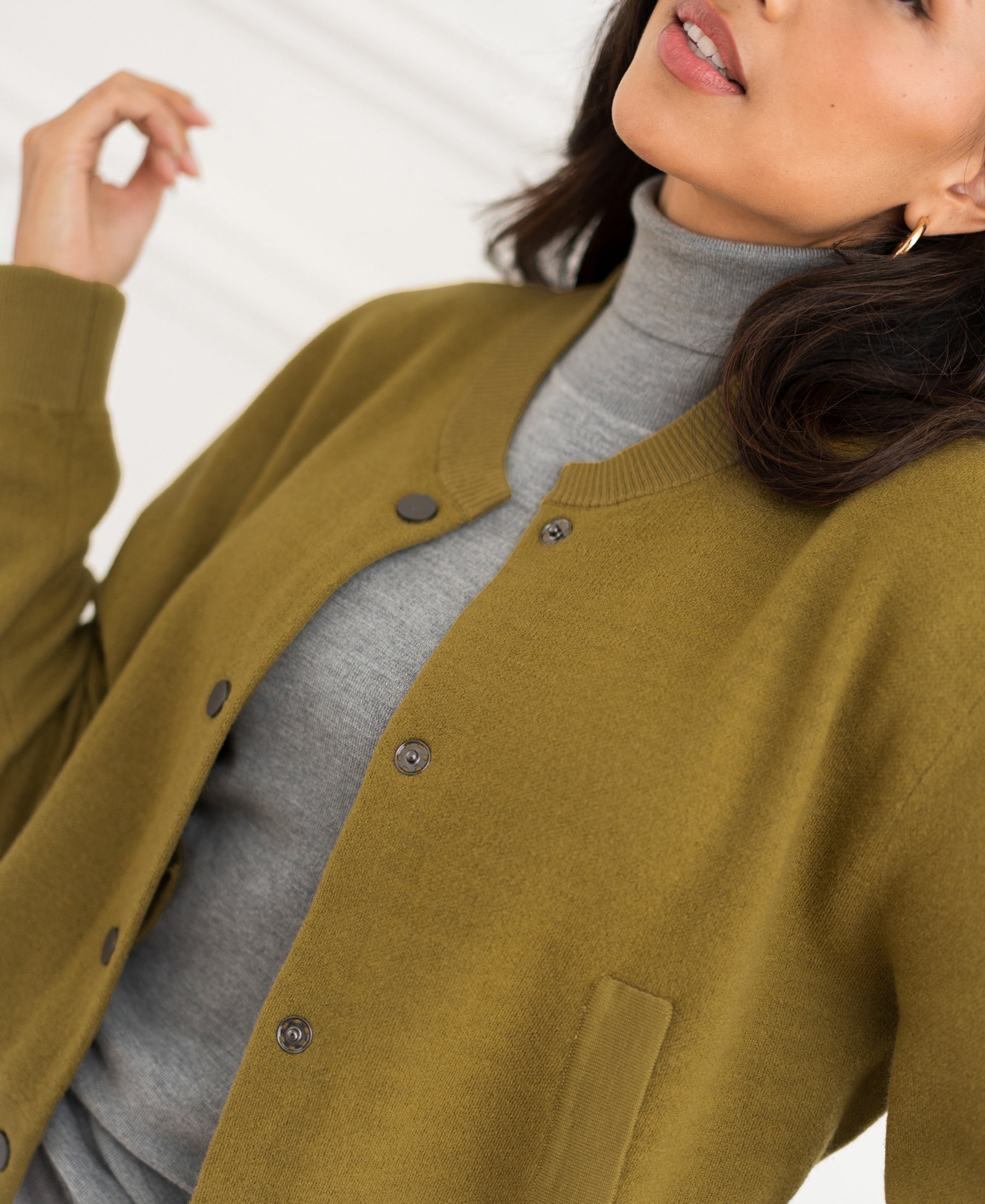 Olive green LA BOMBA bomber jacket by PLEIN PUBLIQUE, shown from shoulders to mouth with one hand raised.