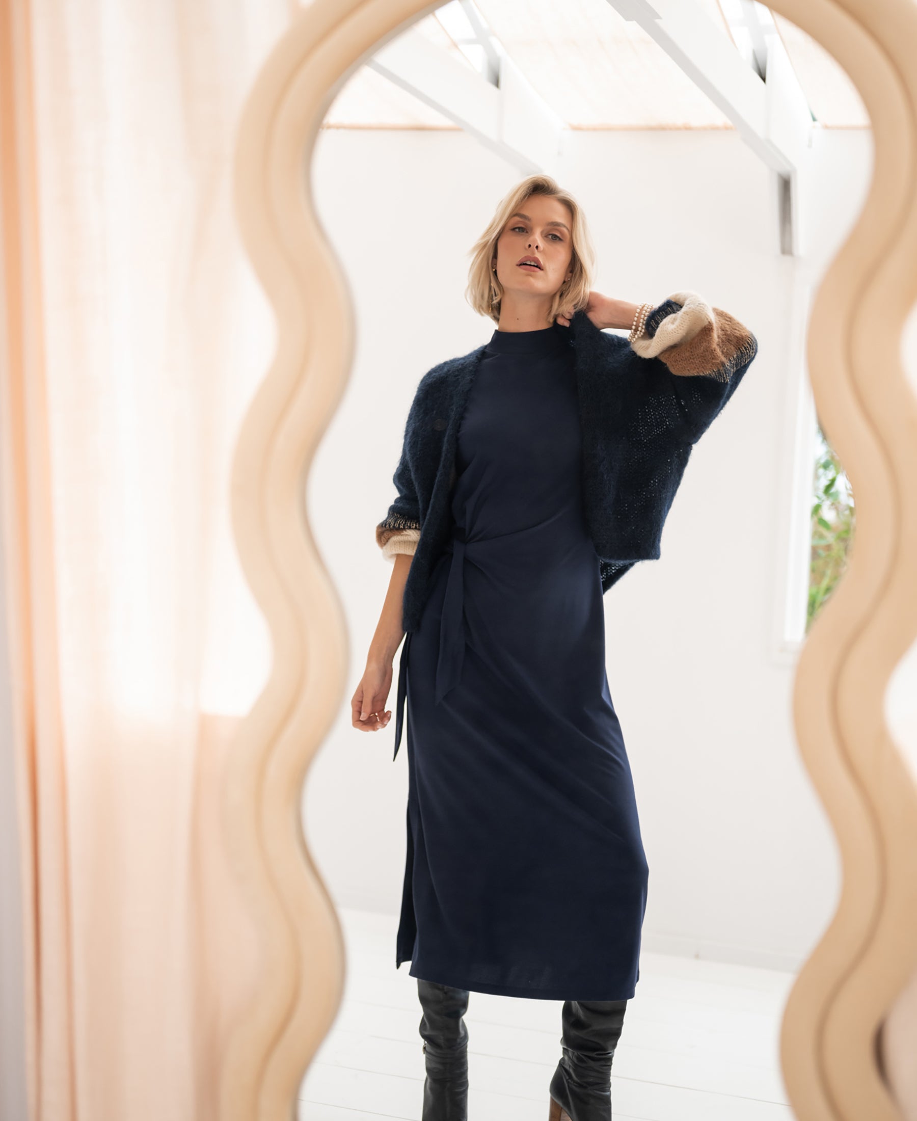 Dark blue LA TOULOUSE travel dress by PLEIN PUBLIQUE shown near a wavy mirror in a stylish room.