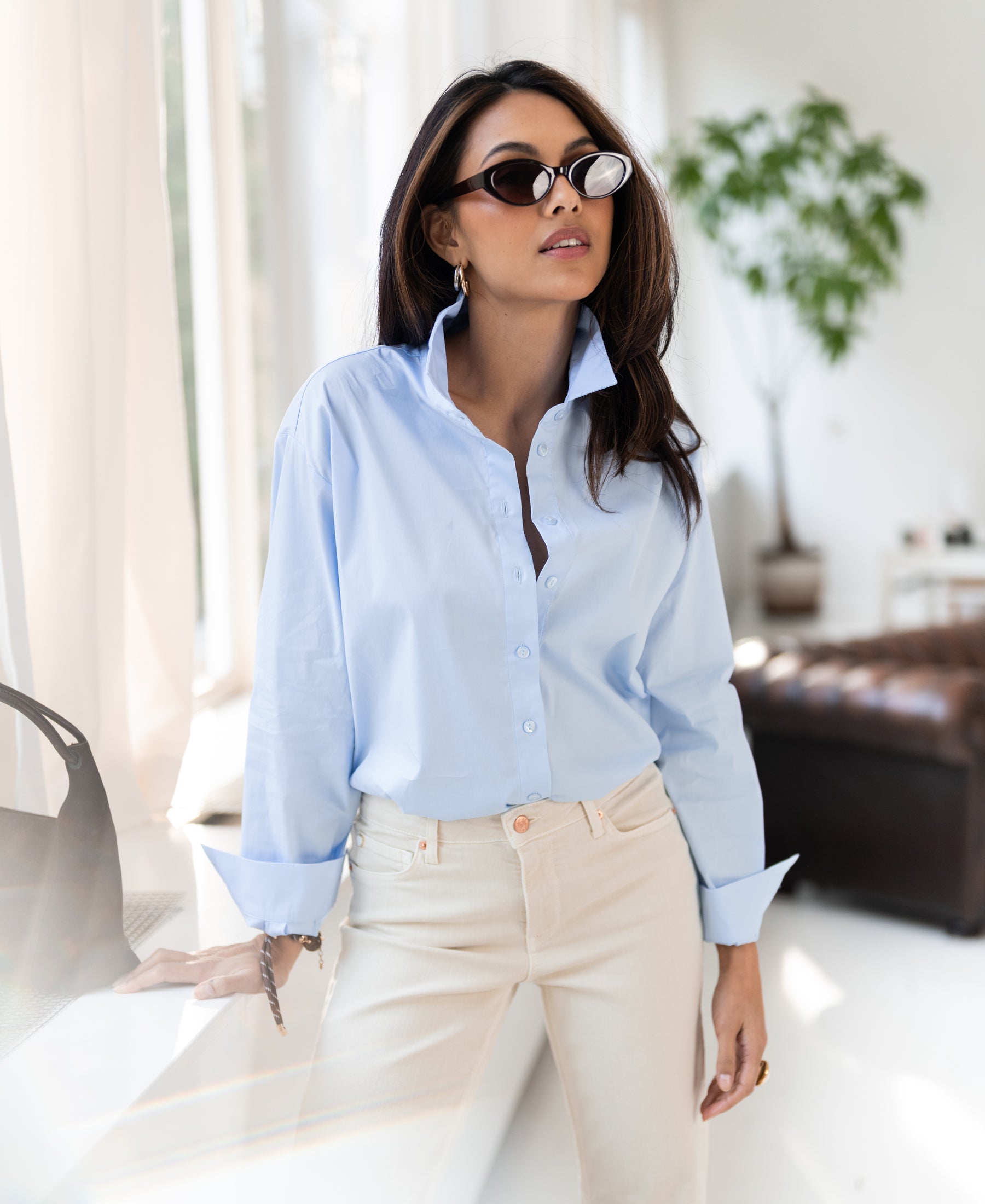 Light blue oversized blouse in cotton, shown indoors near a sunlit window.