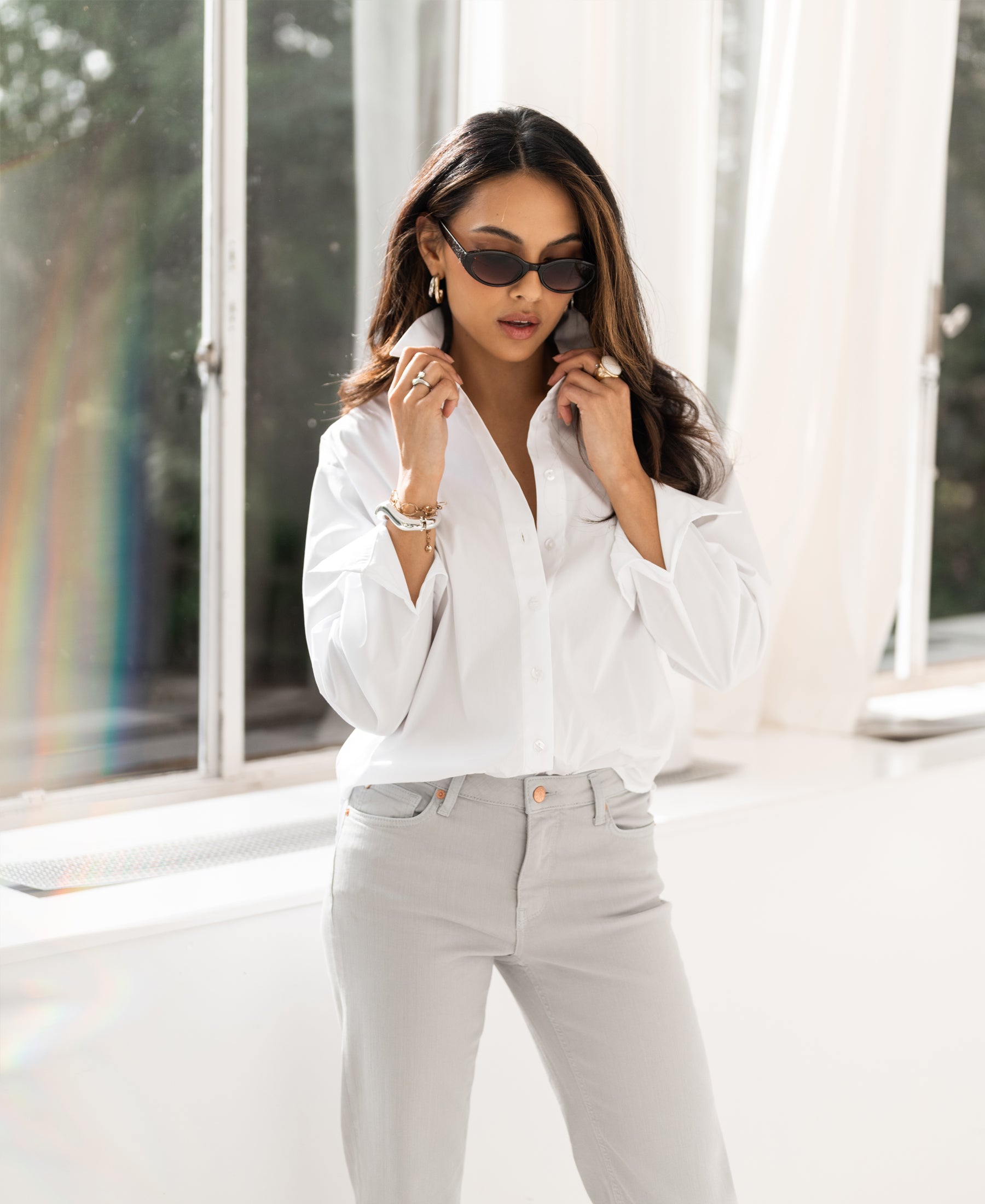 Oversized white blouse, shown as the model adjusts the collar by a window.