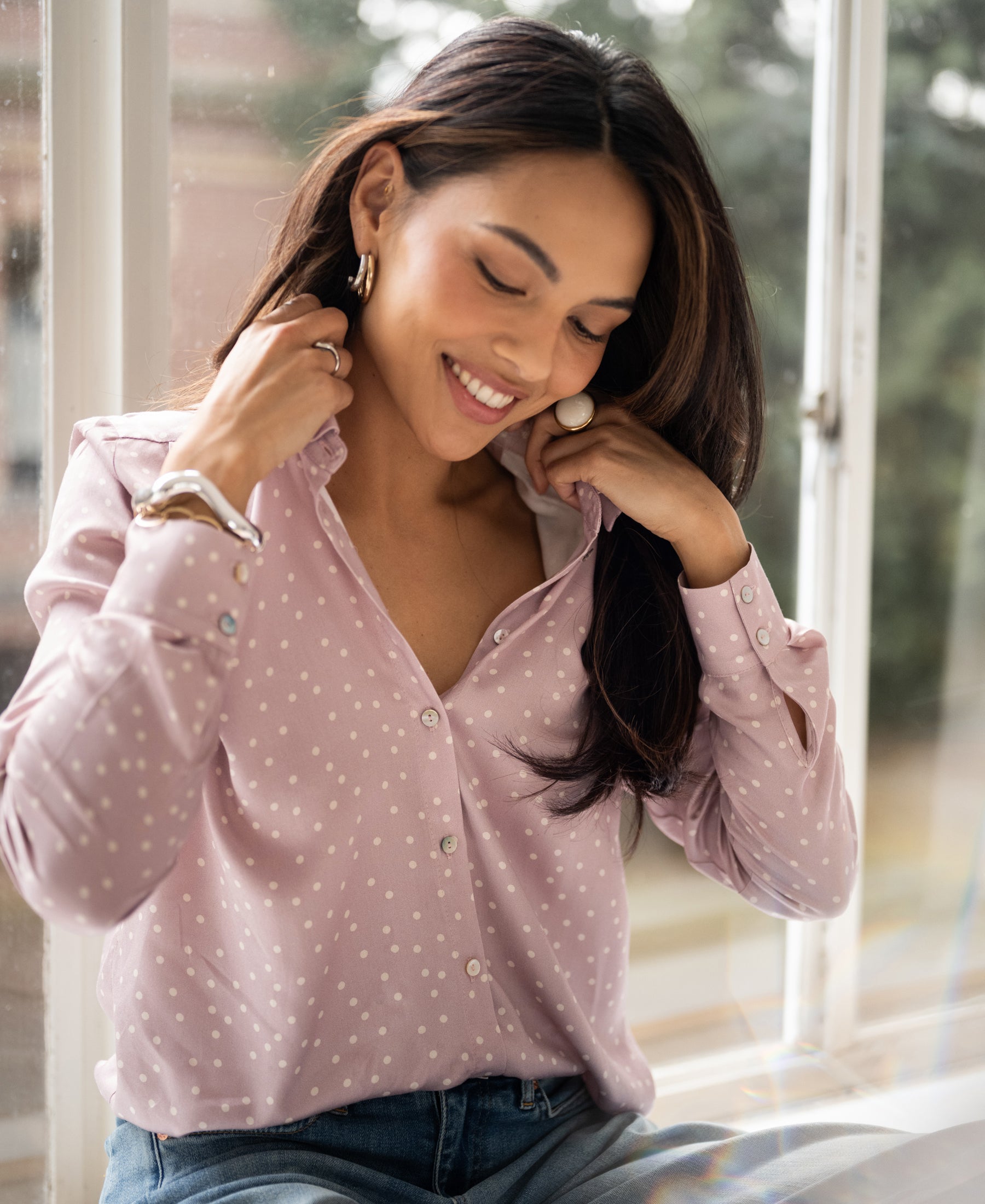 PLEIN PUBLIQUE blouse in dusty pink with ivory dots, shown as the wearer adjusts the collar near a window.