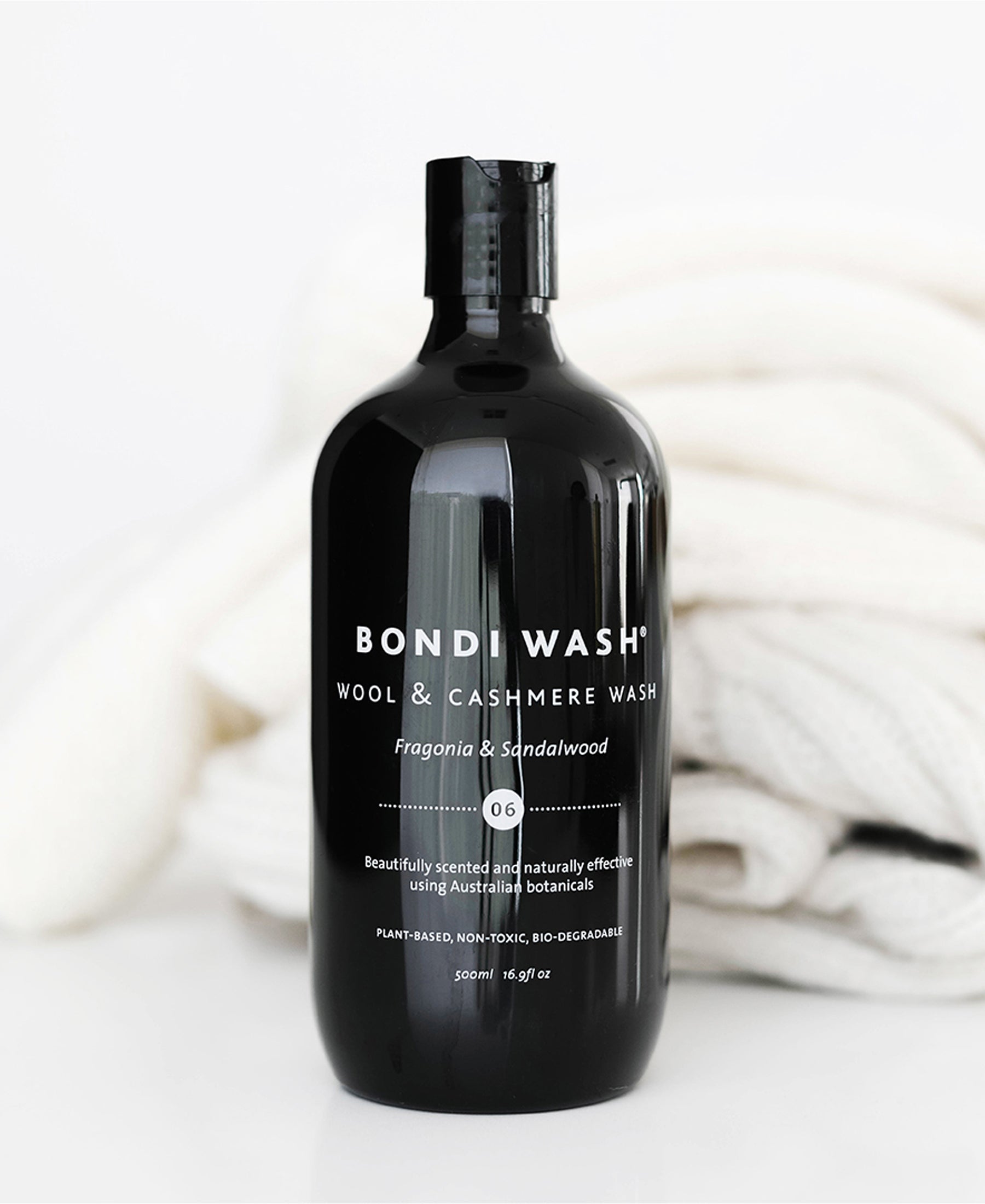 A black bottle of BONDI WASH Fragonia & Sandalwood laundry detergent displayed against folded white fabric.
