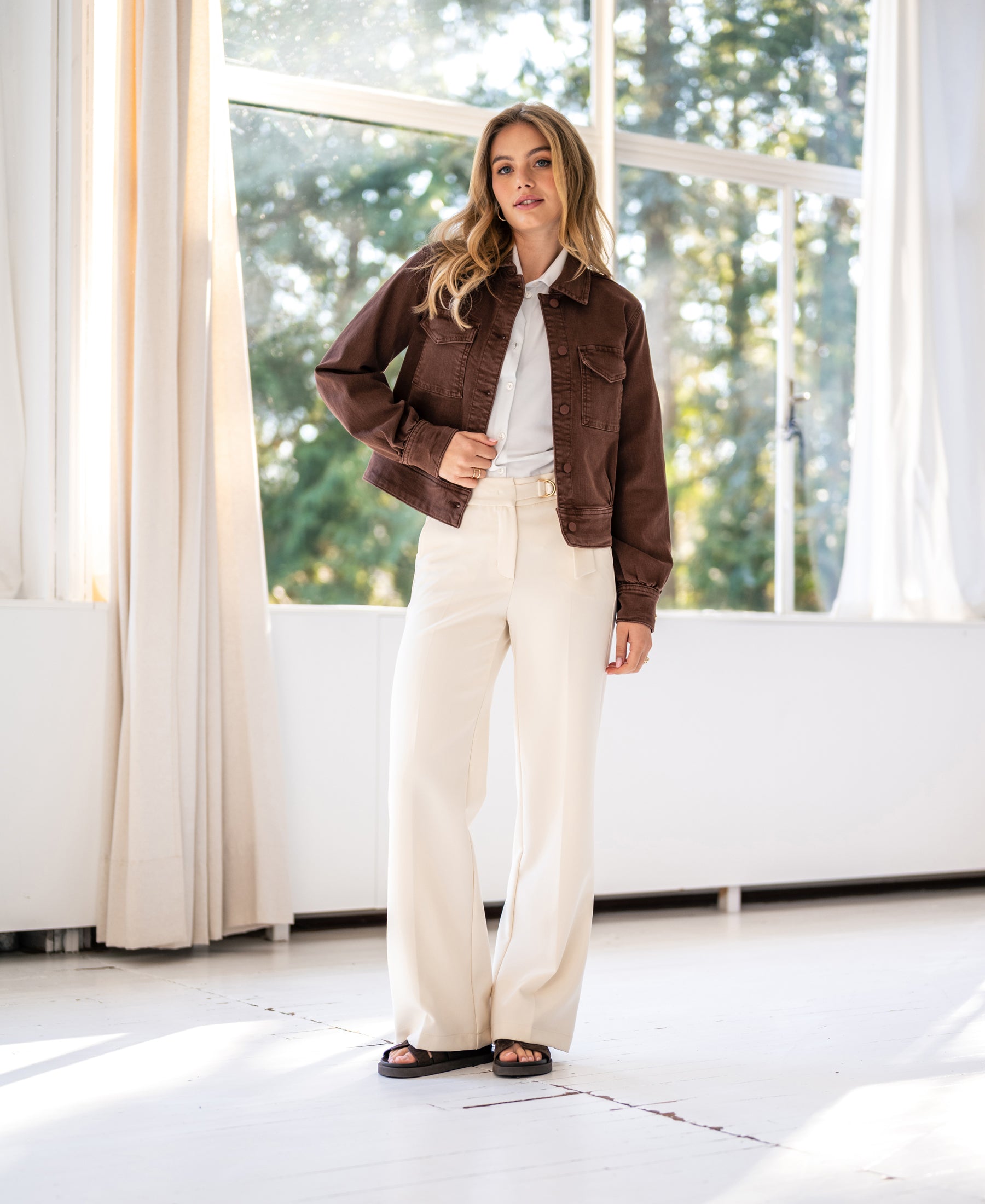 Stretch denim jacket in cacao brown shown indoors with sunlight streaming inside.