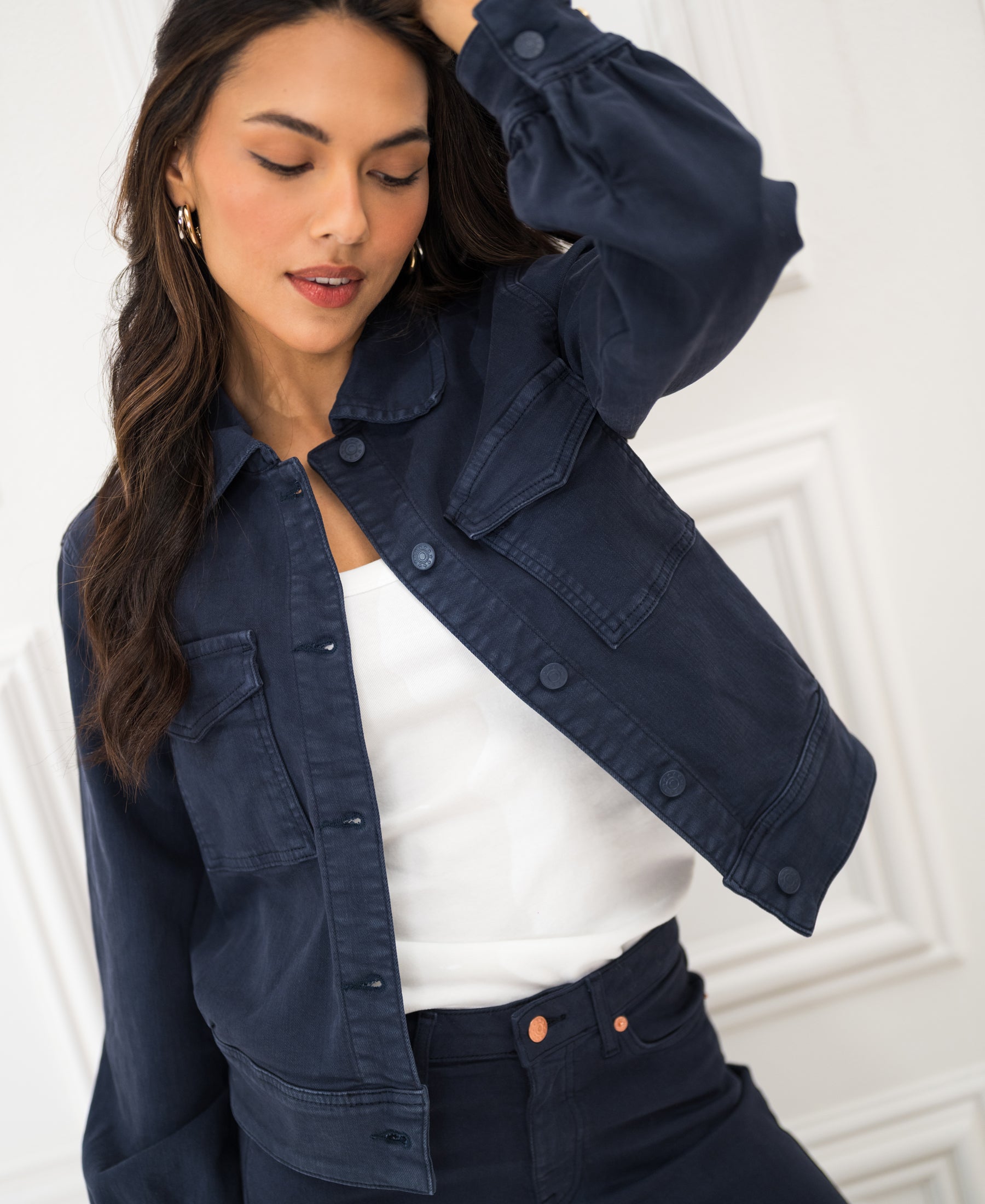Woman wearing a dark blue stretch denim jacket, with one hand on her head.
