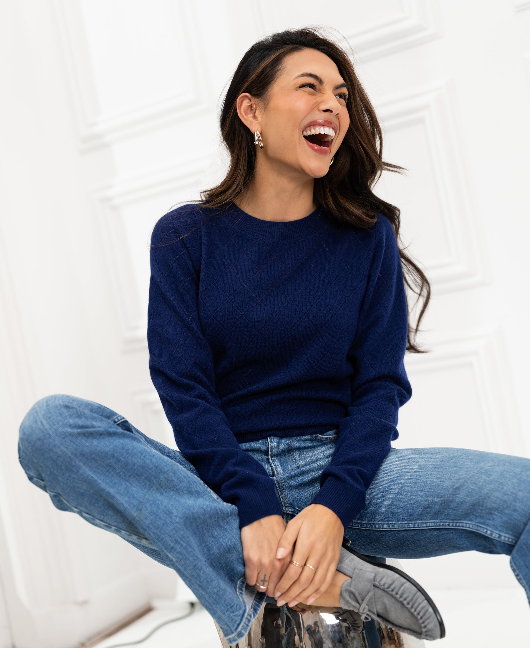 Navy argyle merino wool sweater, front view, shown worn by a woman seated cross-legged against a white panel.