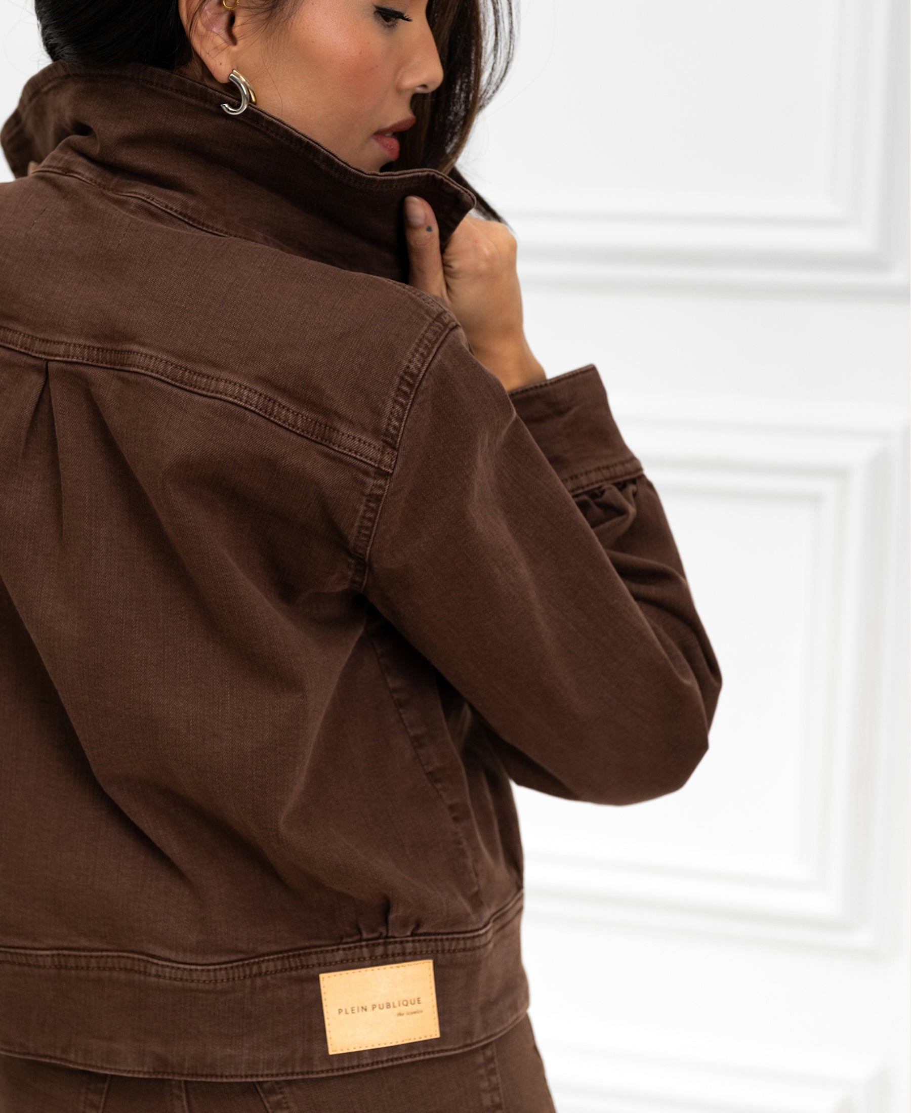 Stretch denim jacket in cacao brown, shown from the side with the collar held near the model's face.