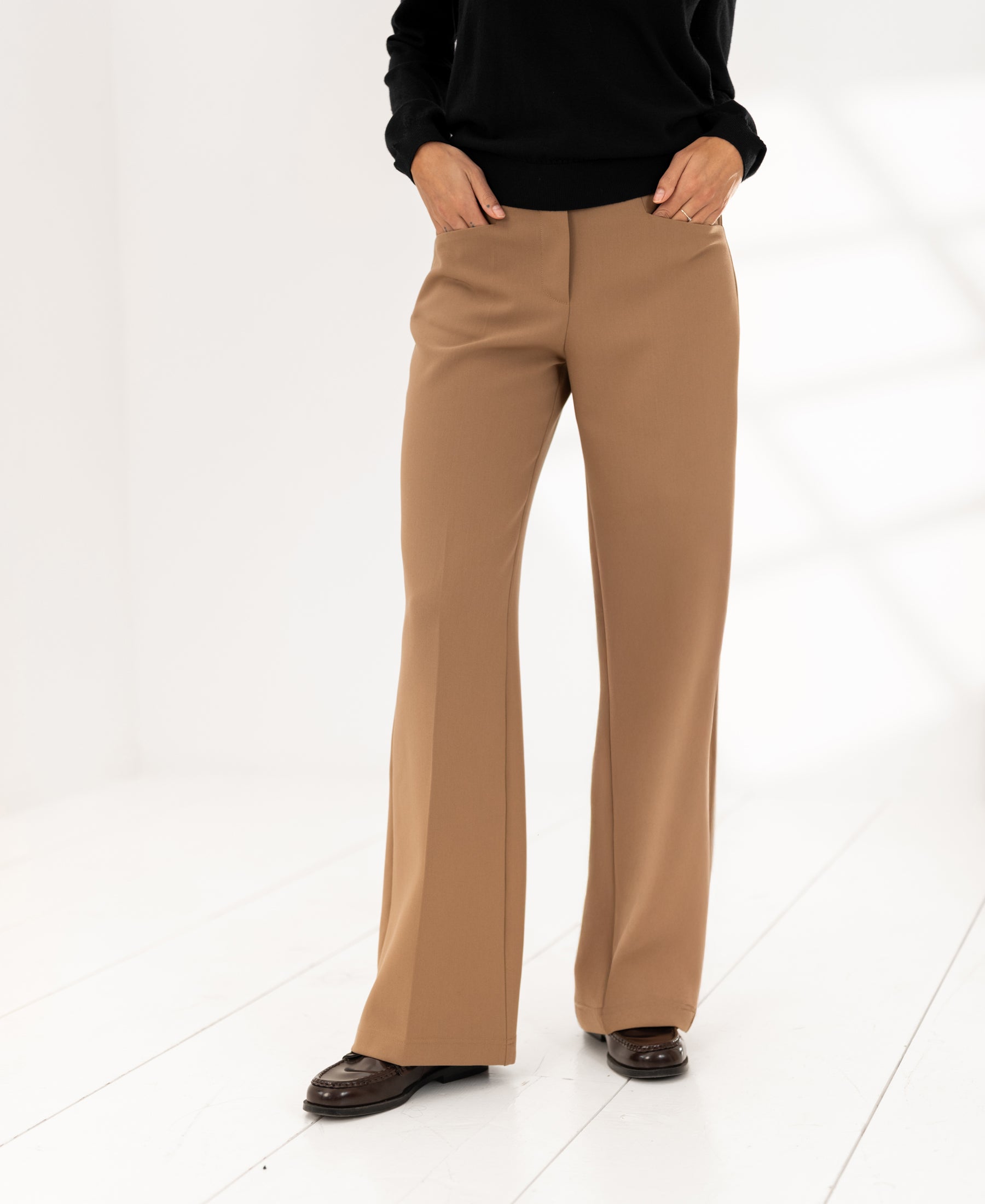 Person draagt de PLEIN PUBLIQUE wide-leg trousers LE CENTRE in camel in een lichte kamer.