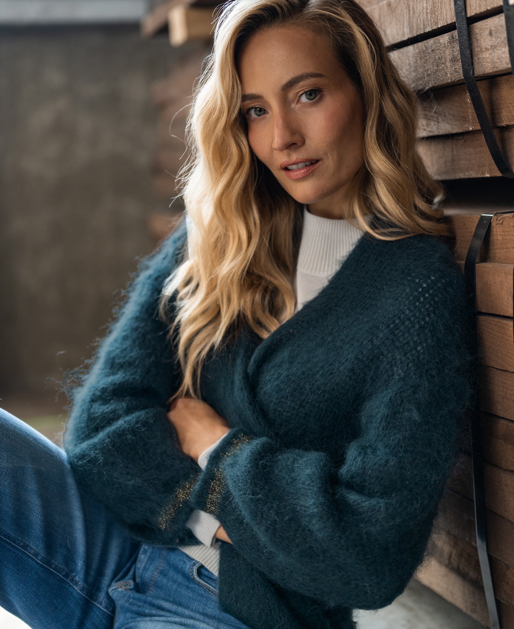 PLEIN PUBLIQUE Fluffy vest LA CHERIE in dark mist green, shown by a woman with long wavy blonde hair by wood planks.