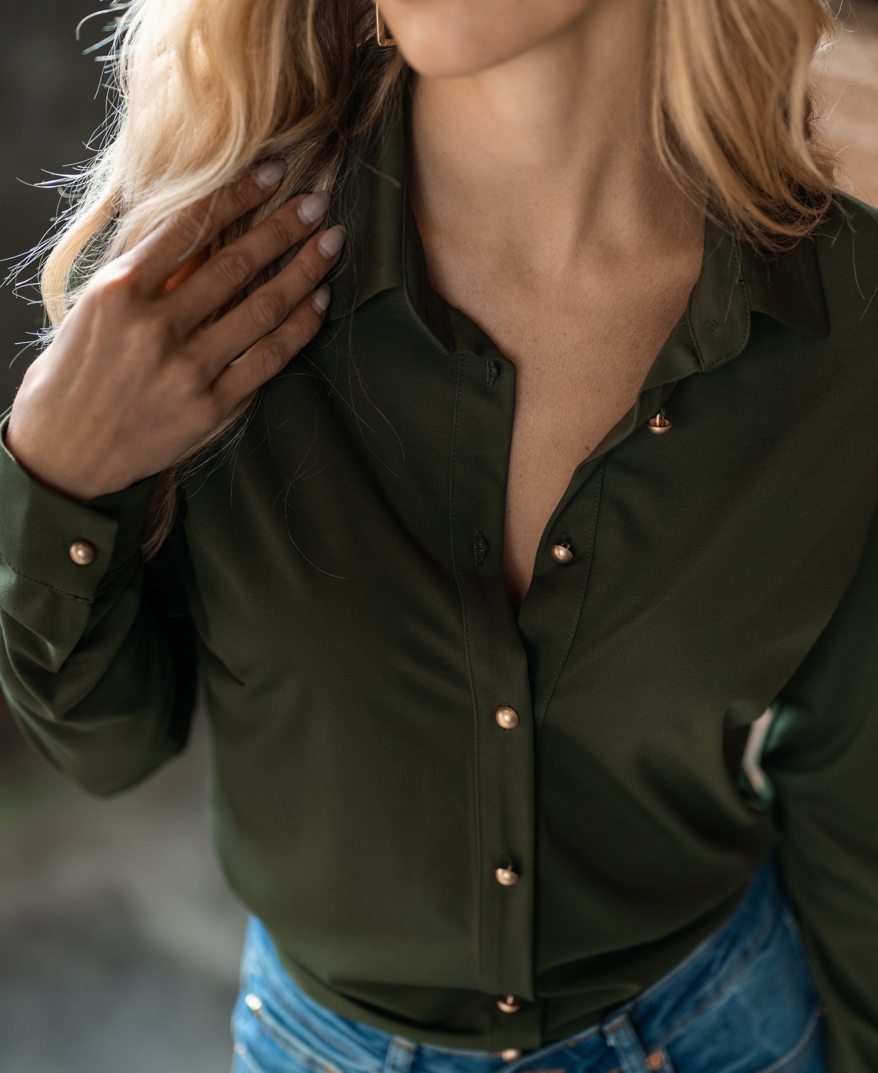 Woman wearing the PLEIN PUBLIQUE Travel blouse LA CHERISE in army green with gold buttons, touching her hair.