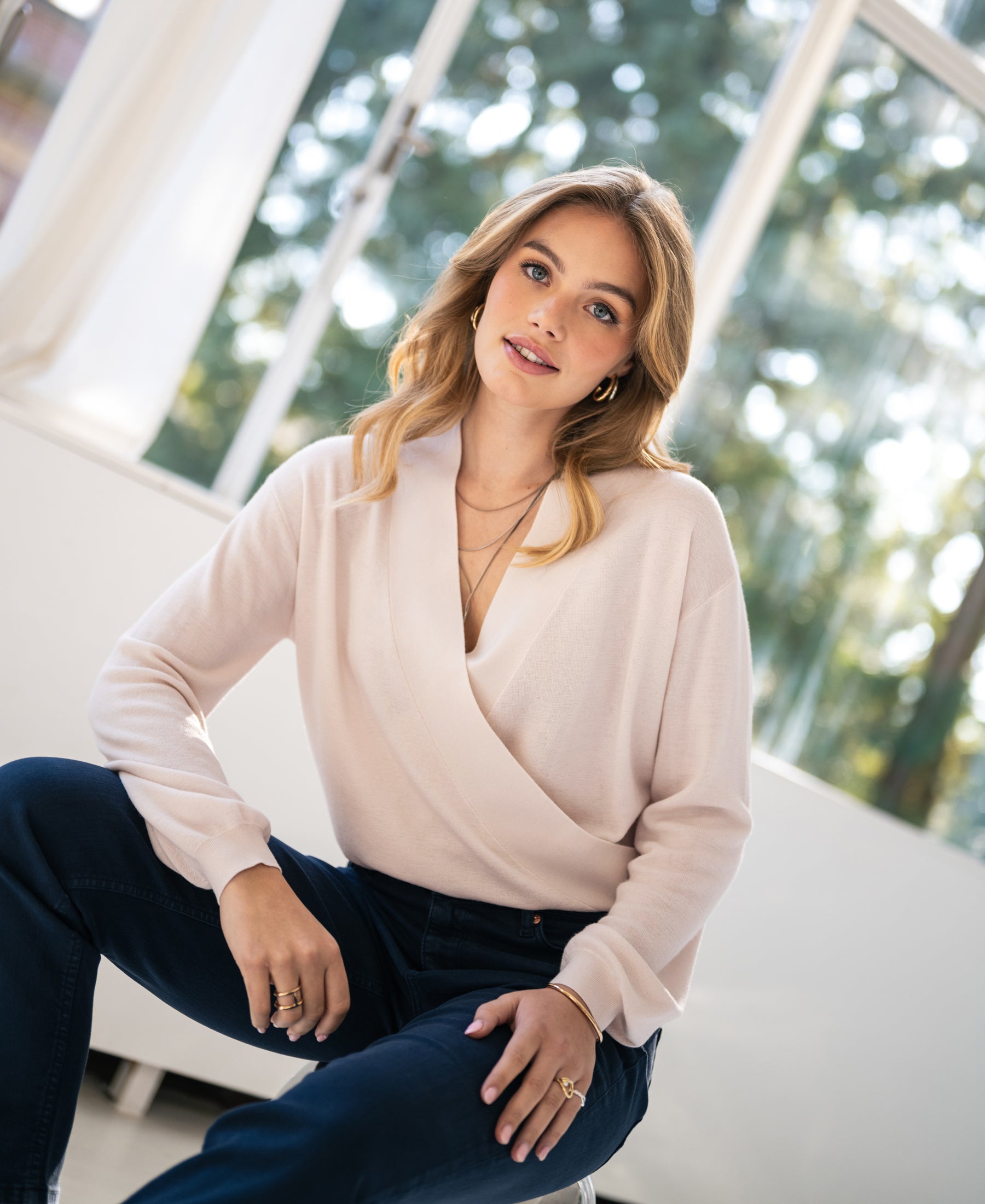 Soft blush wrap sweater in knit fabric from PLEIN PUBLIQUE, shown by a window.