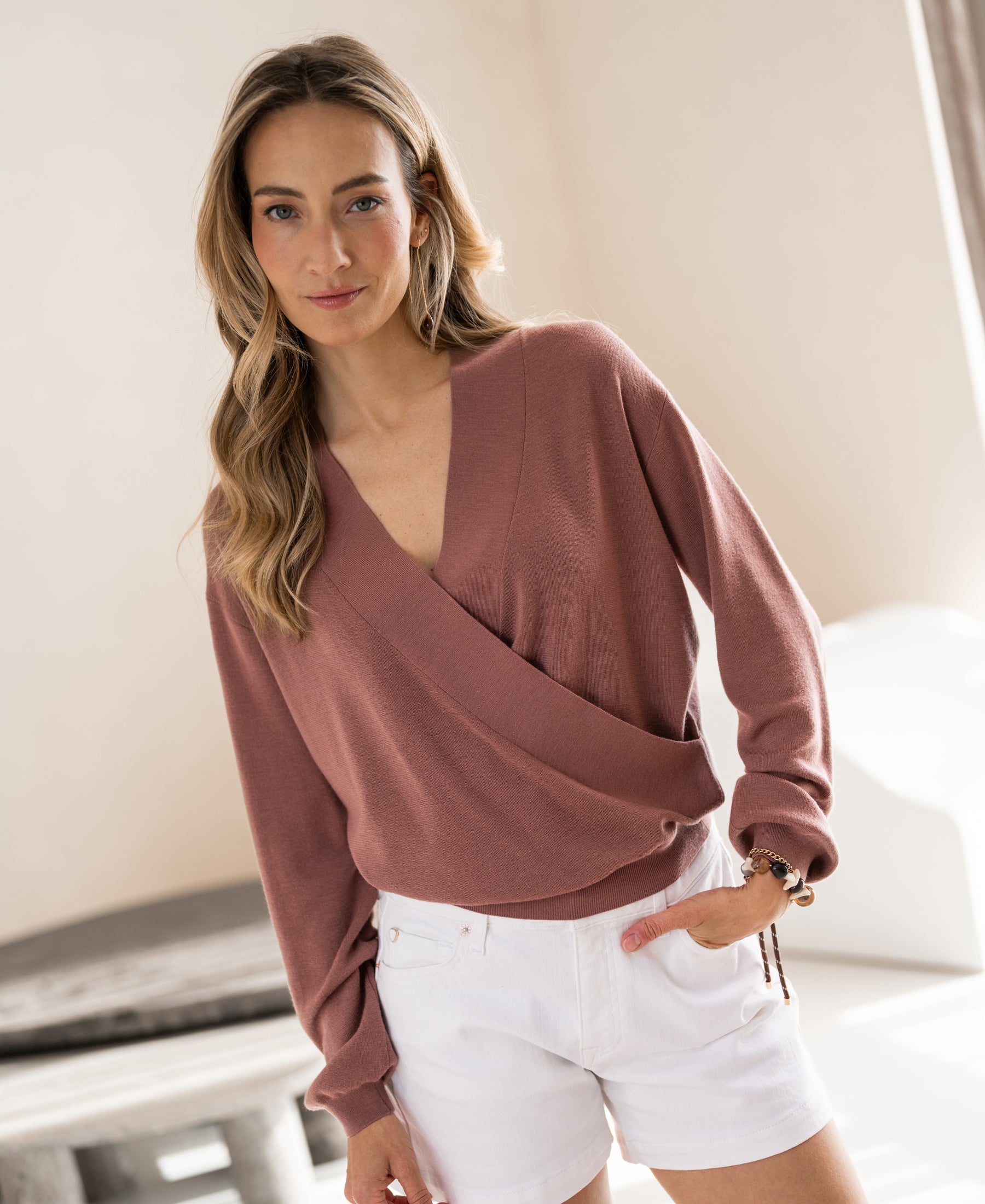 Dusty pink PLEIN PUBLIQUE wrap sweater LES CINQ, shown worn indoors by a woman with long wavy hair.