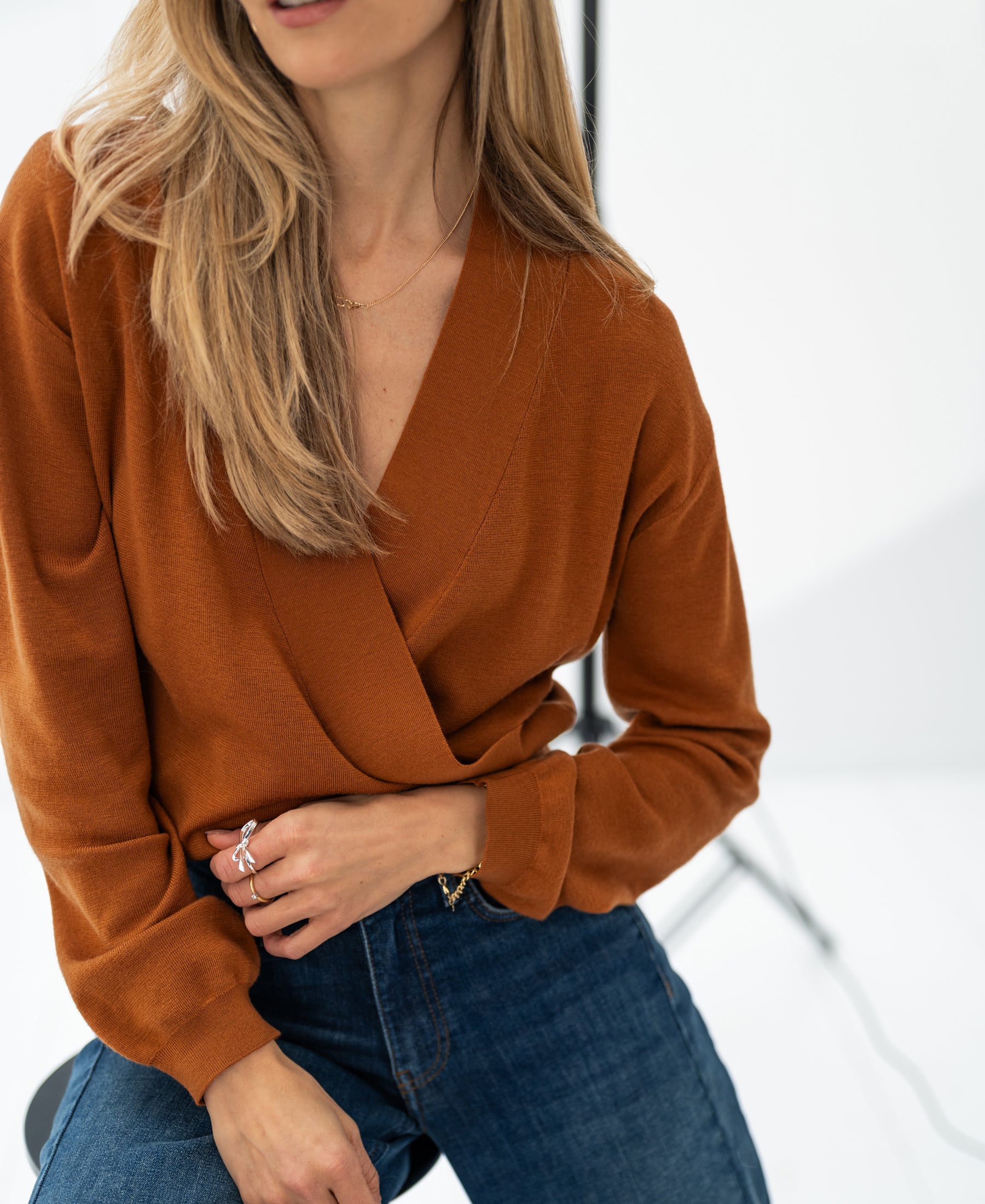 Vrouw poseert in lichte studio met hand op heup in terra-kleurige LES CINQ wraptrui van PLEIN PUBLIQUE.