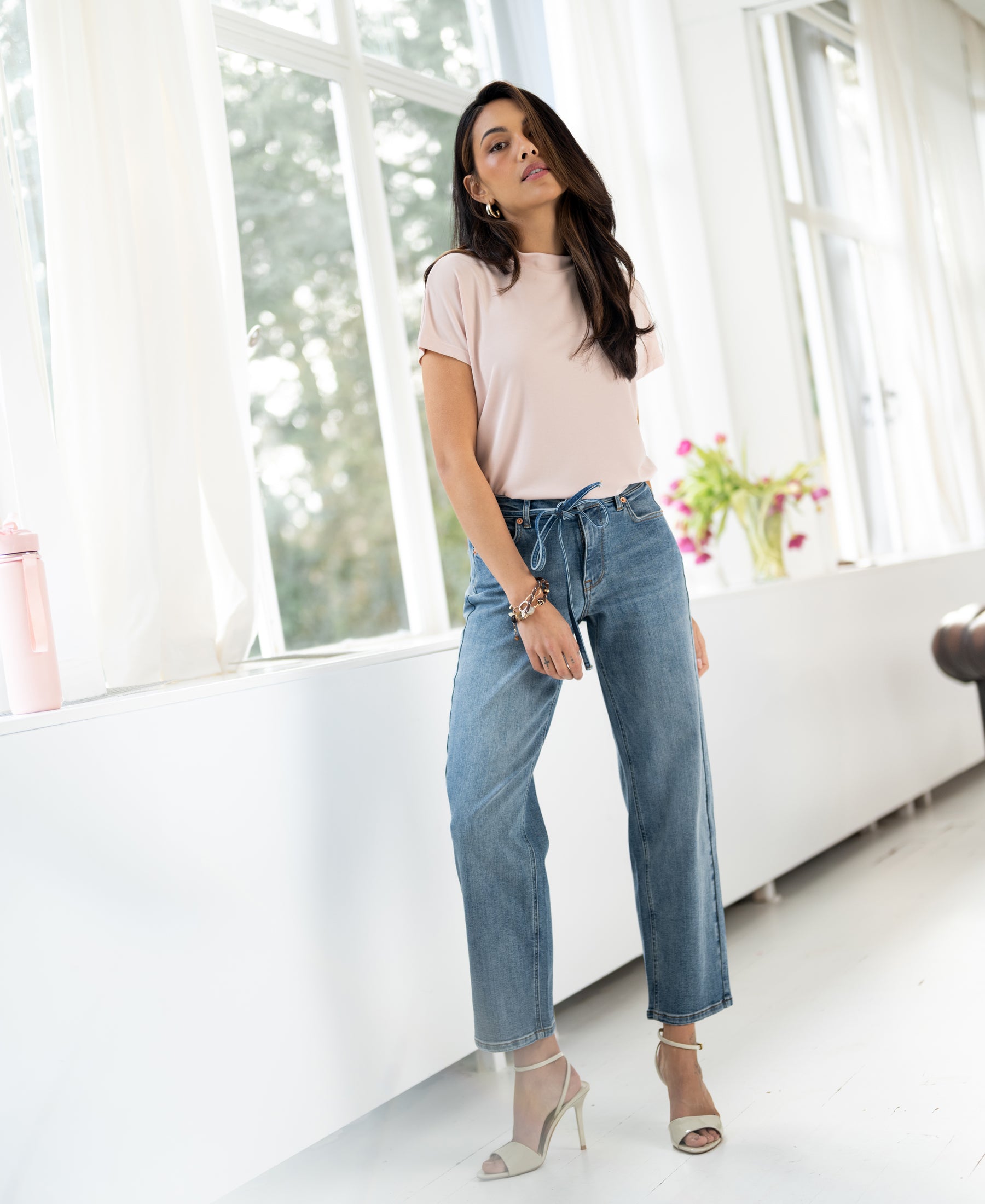 Light stone-wash cropped jeans in a classic fit, shown indoors by large windows.