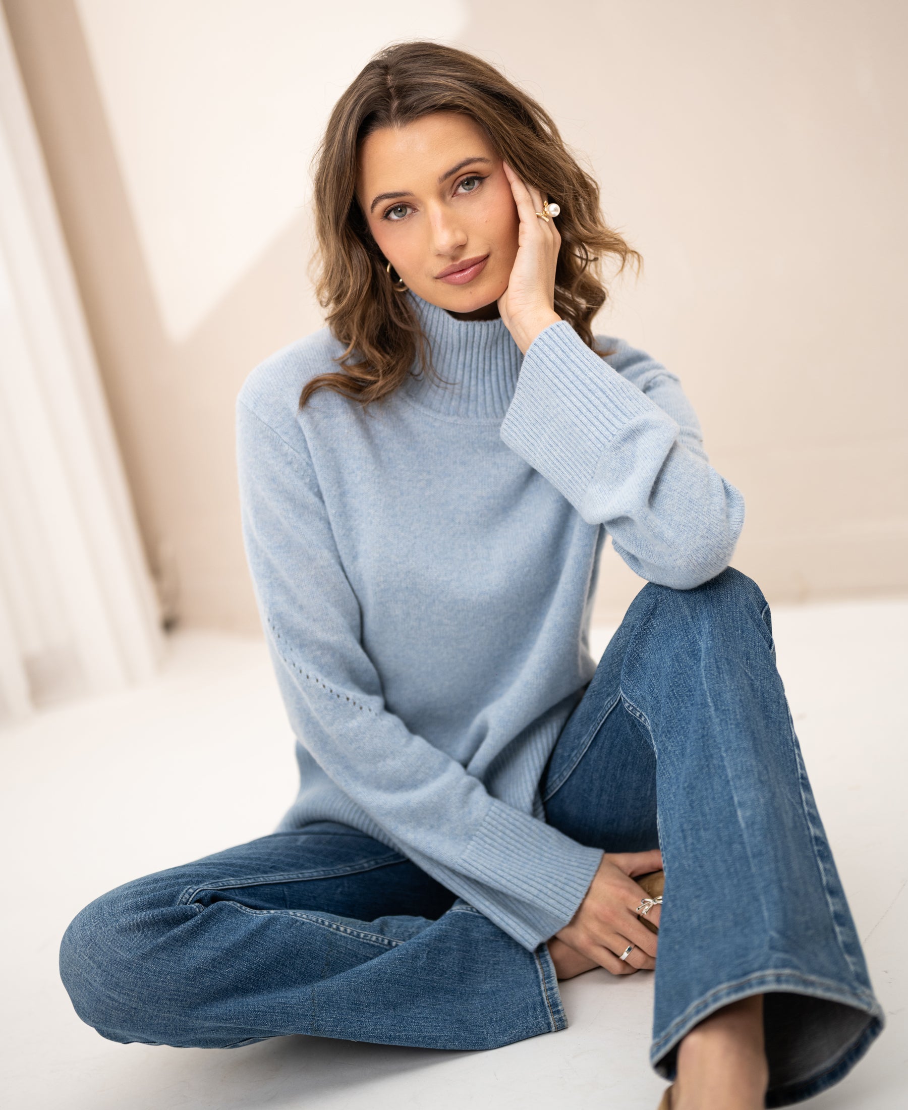 Light blue PLEIN PUBLIQUE LA COZY turtleneck sweater shown on a woman sitting on the floor, front view.