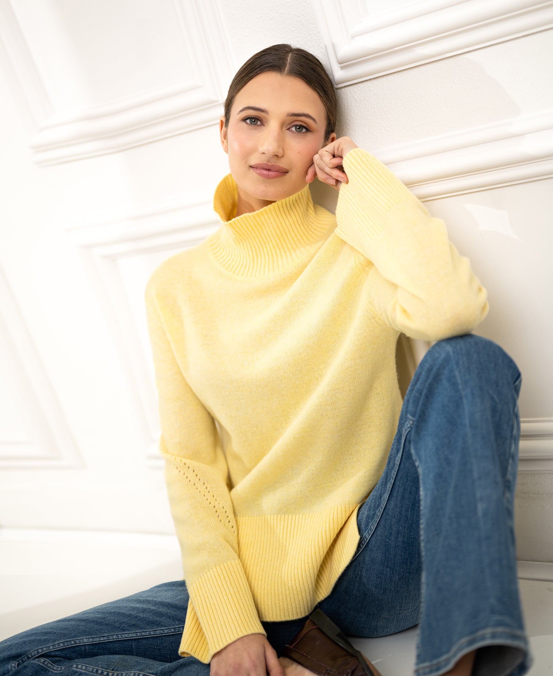 Woman wearing PLEIN PUBLIQUE's LA COZY lemon yellow turtleneck sweater, sitting and smiling.