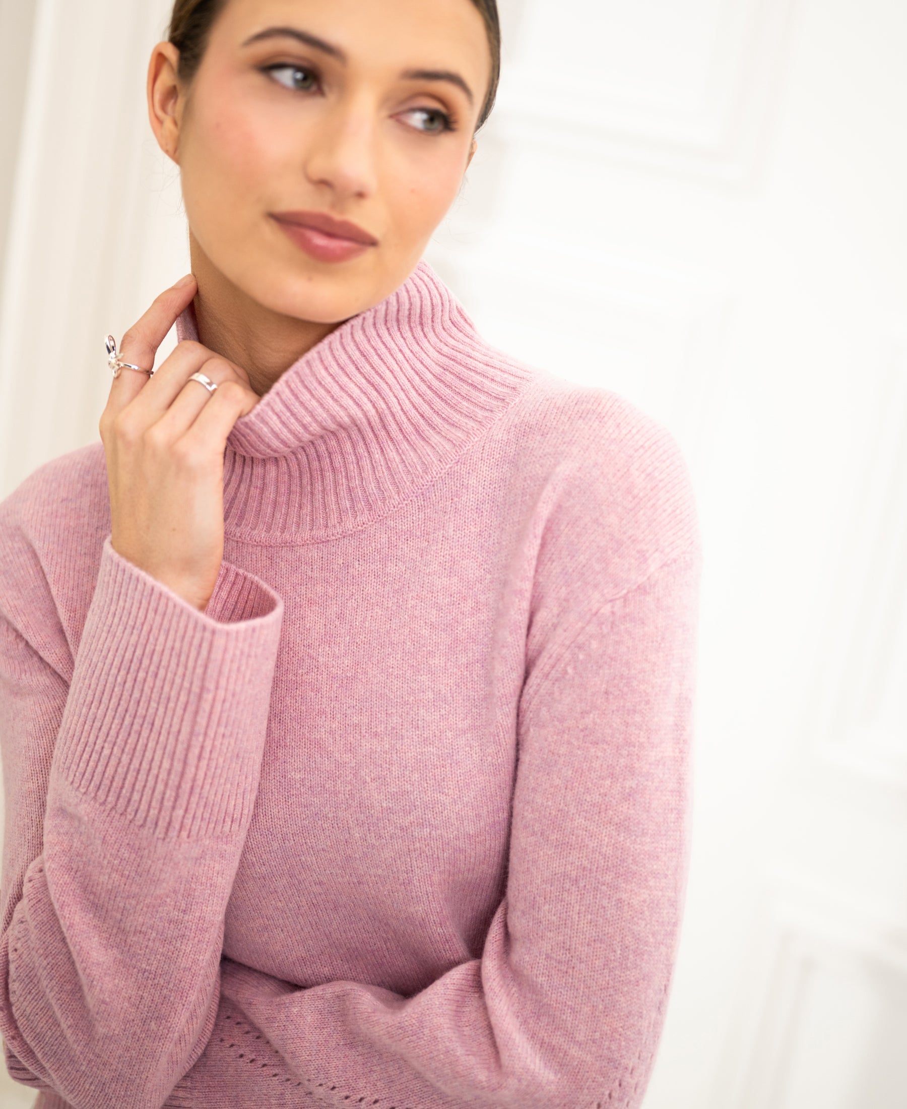 Woman wearing a pink PLEIN PUBLIQUE LA COZY turtleneck sweater, shown from the side.
