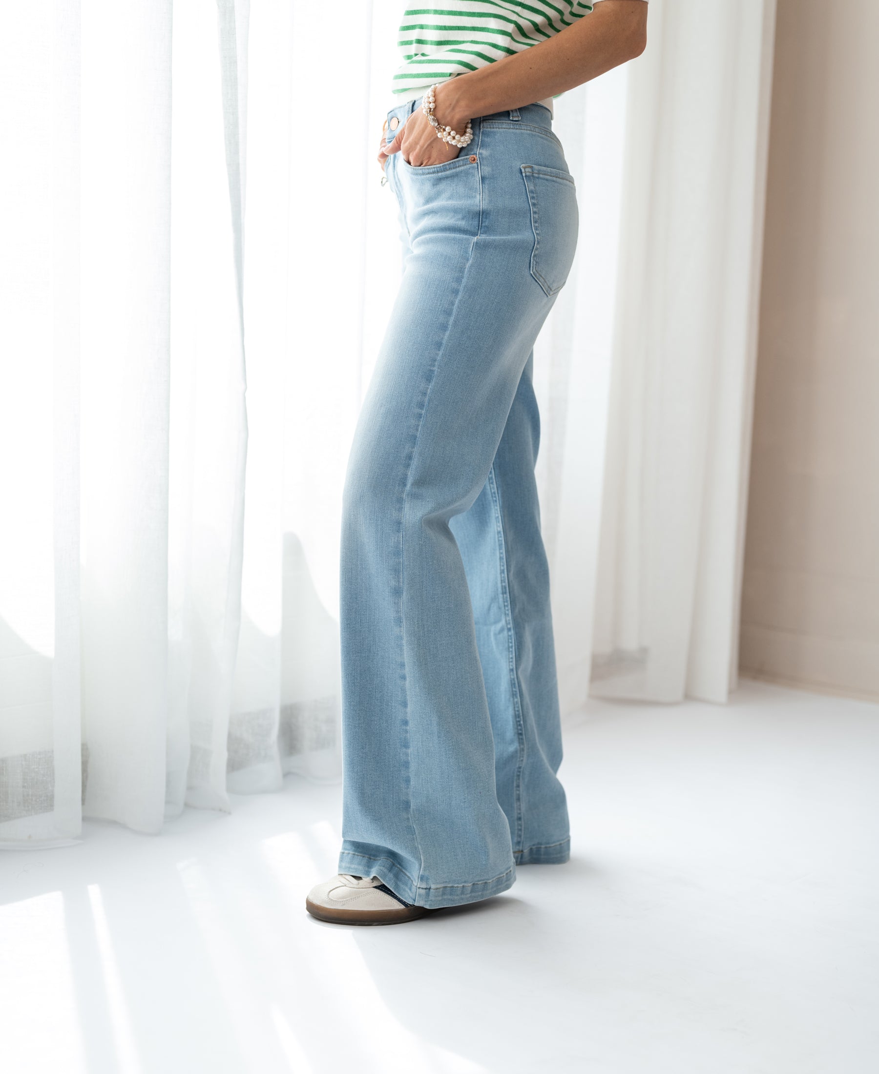 Bleached PLEIN PUBLIQUE wide leg jeans shown in sunlight by white curtains.