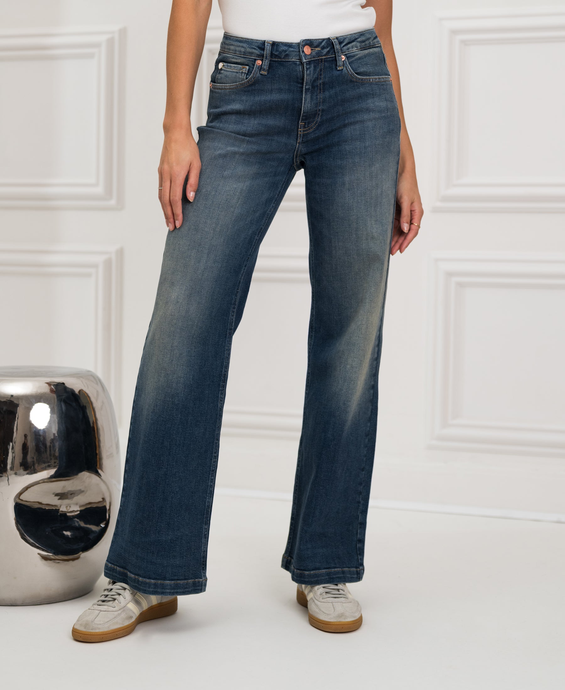 Person wearing wide leg blue vintage jeans by Les Deux, standing indoors near a silver decor object.
