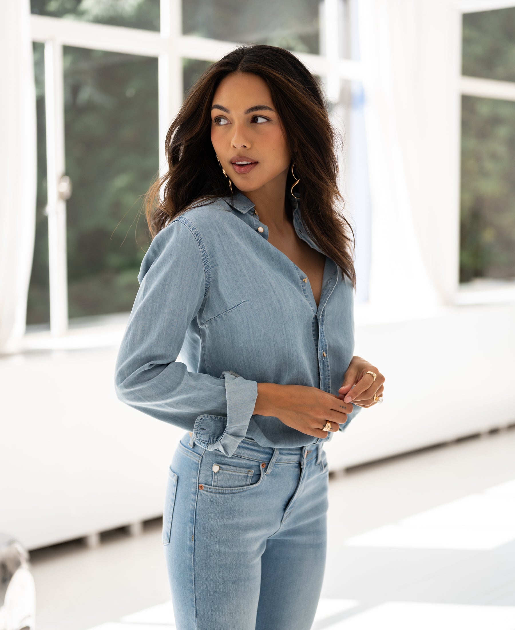 Woman wears light blue Tencel denim blouse, standing indoors in natural light.