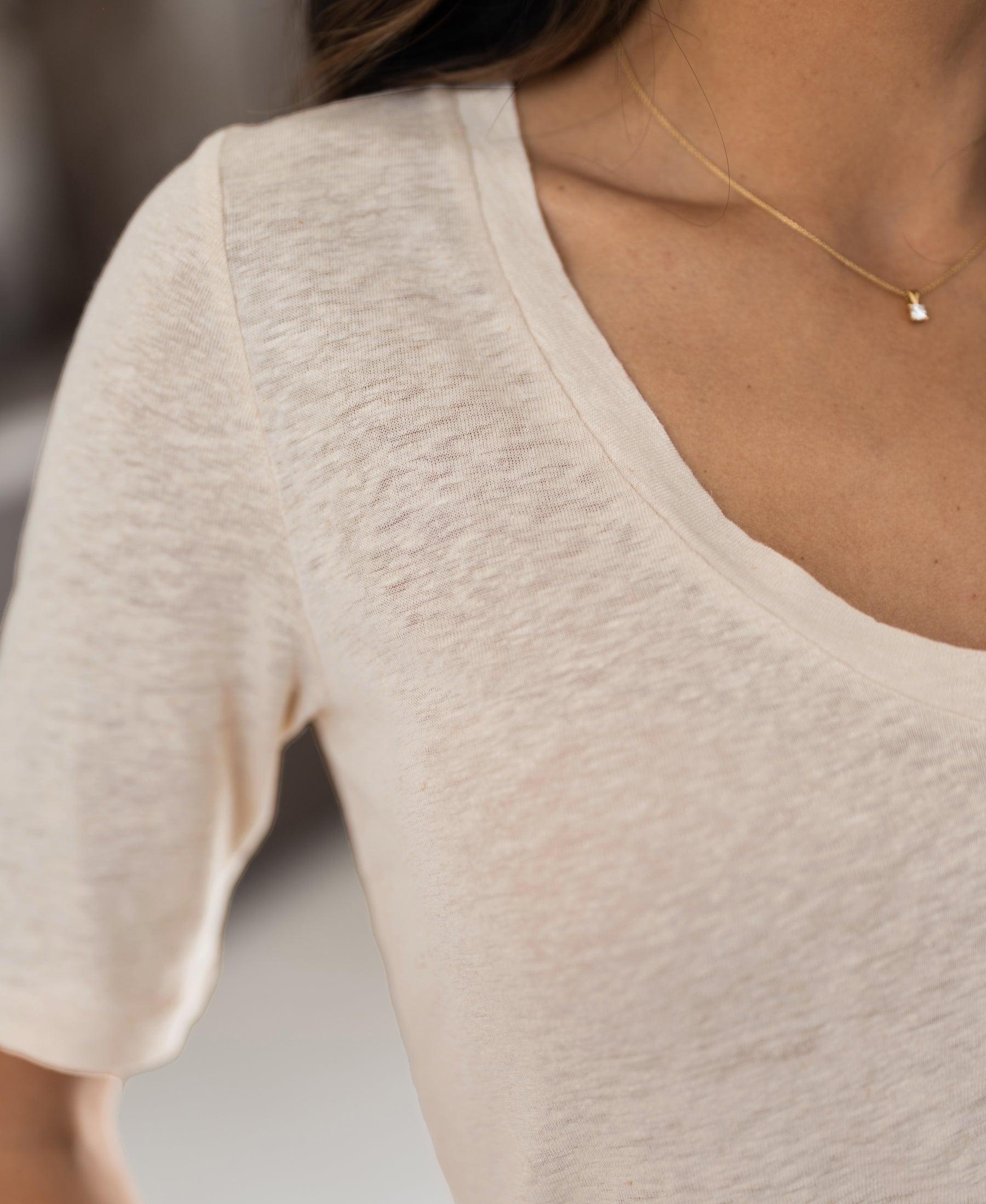 Close-up of a person wearing a cream-colored linen T-shirt from PLEIN PUBLIQUE, LA DOMI style.