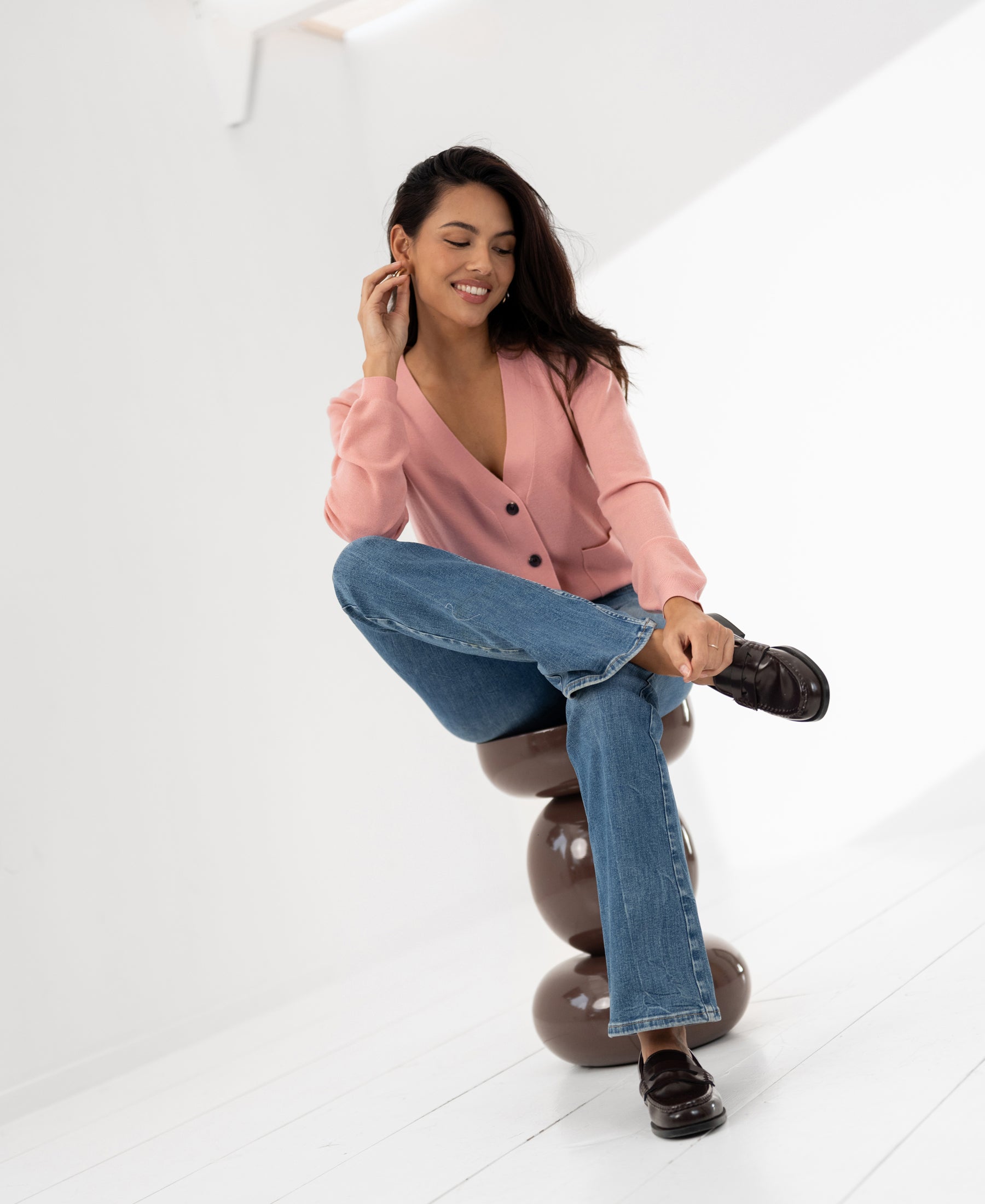 Pink merino wool vest in a bright room, shown on a model sitting and smiling.