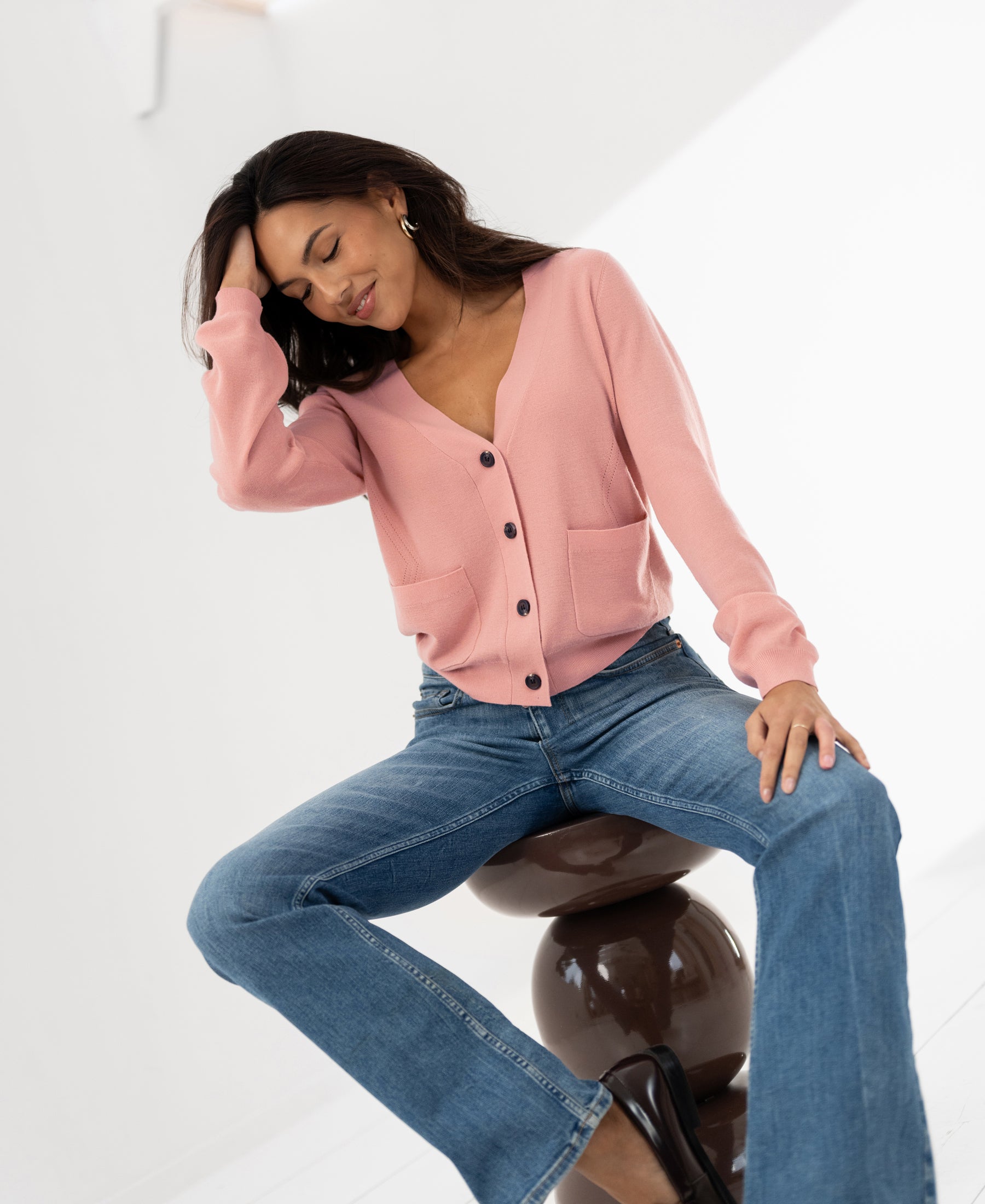 Woman wearing a PLEIN PUBLIQUE LA DONNA pink merino wool cardigan, seated and smiling.