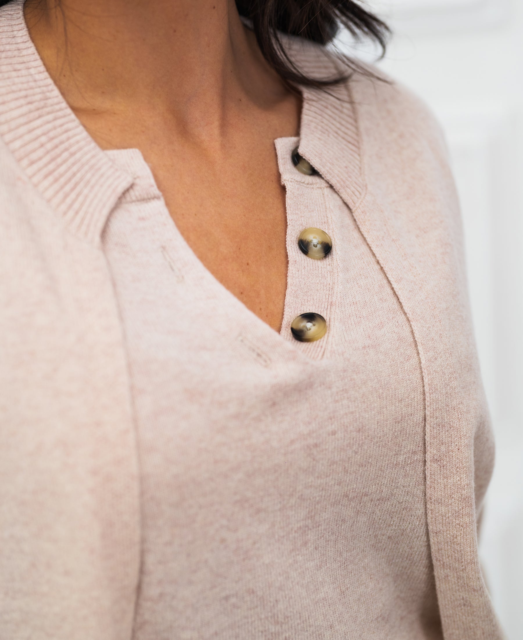 Close-up of light pink merino wool V-neck cardigan with three brown buttons.