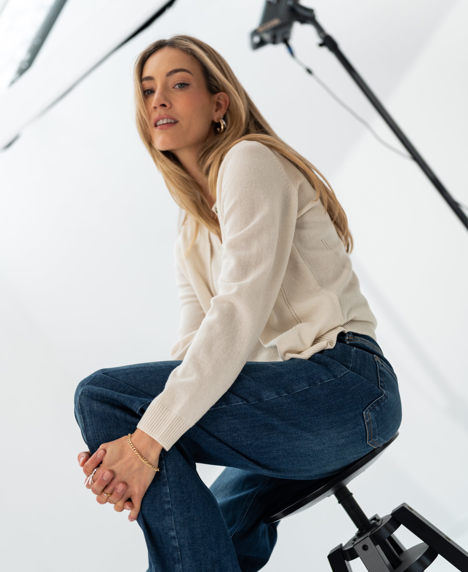 Ivory knit vest with double-layer detail, shown worn by a woman seated on a stool in a modern studio setting.