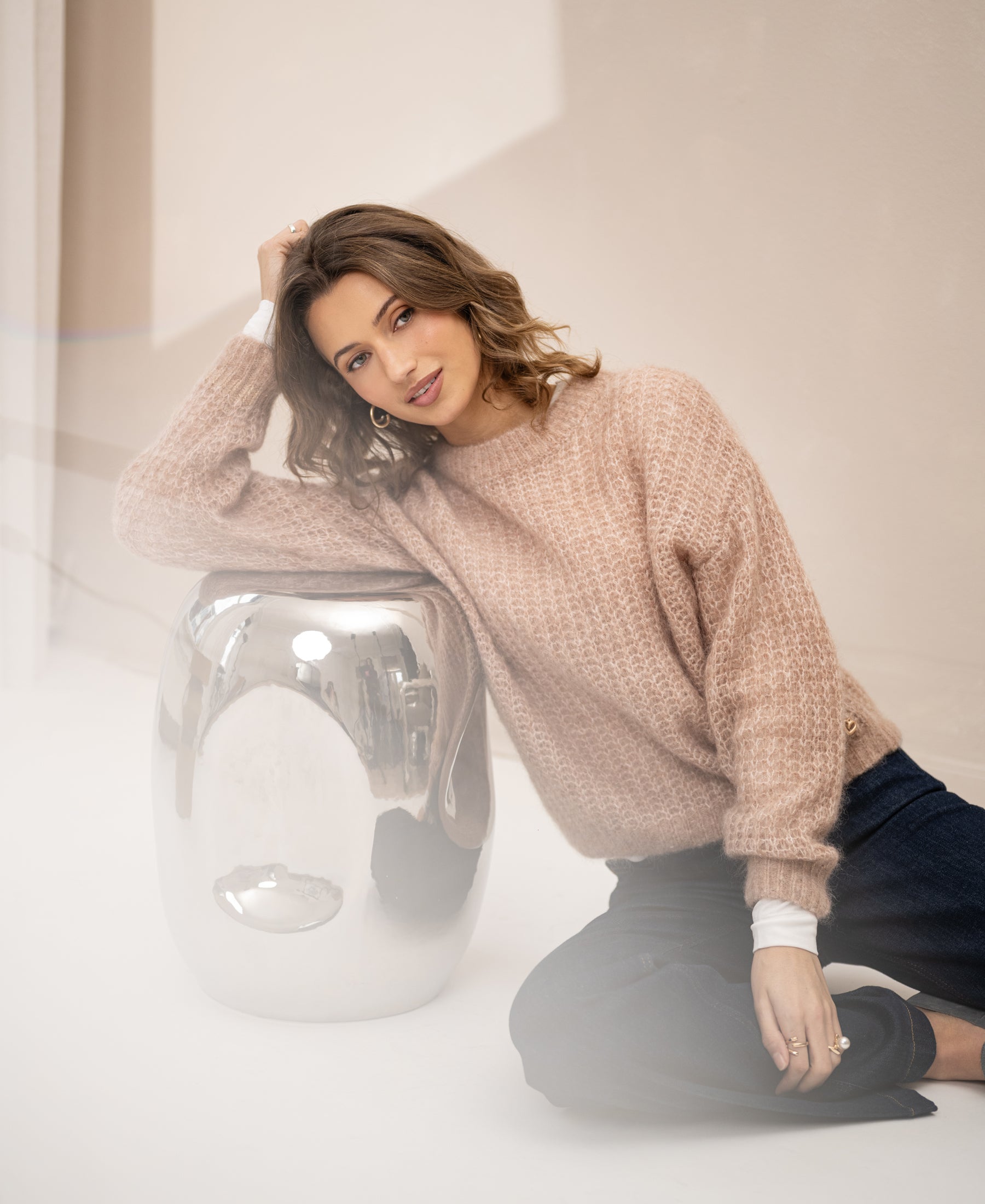 Woman wearing the LA DOUCE Fudge mohair sweater sits on the floor, smiling at the camera.