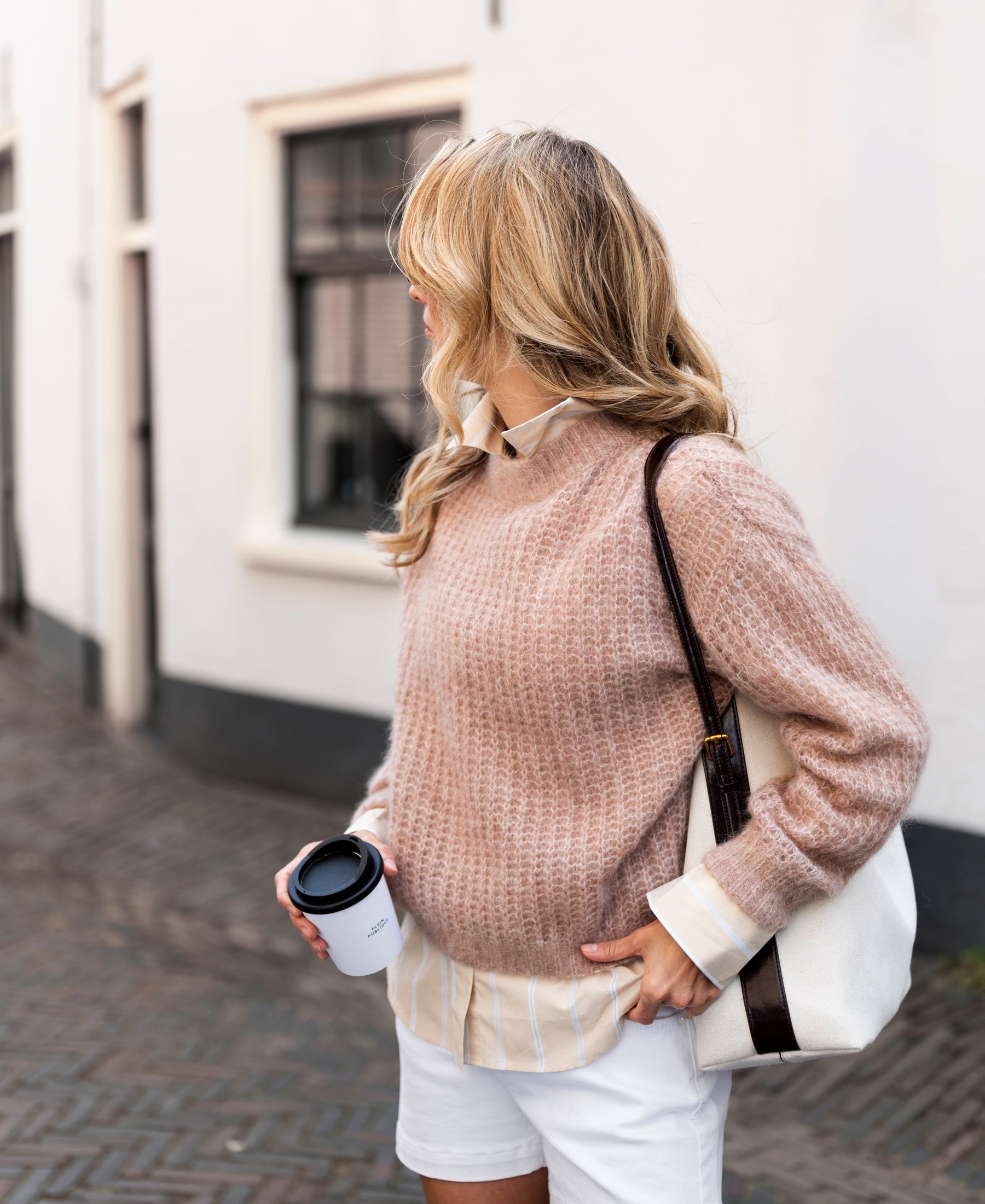 Blonde woman wearing PLEIN PUBLIQUE's mohair sweater in light brown, standing on a city street.