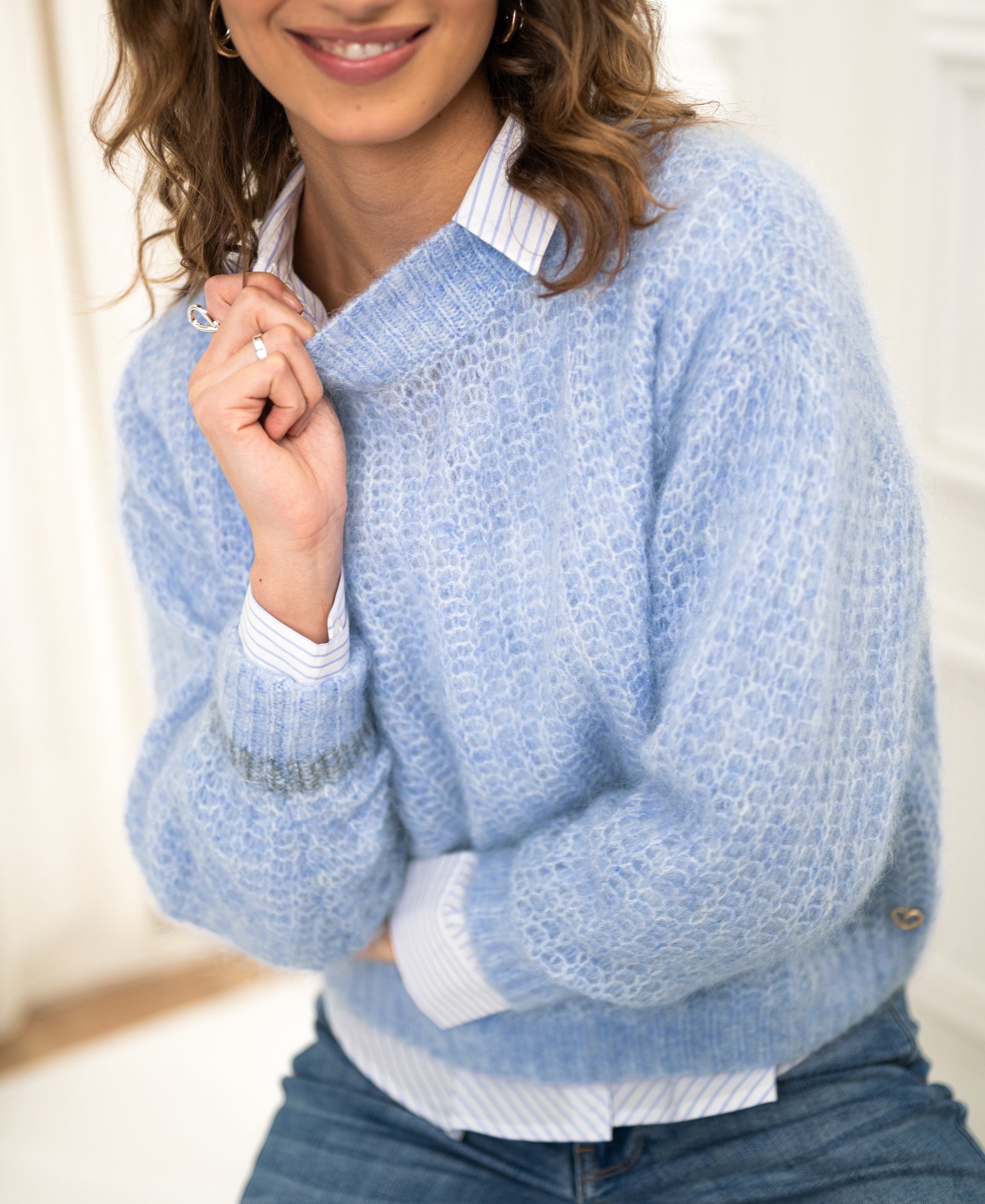 Woman wearing the light blue Mohair sweater LA DOUCE by PLEIN PUBLIQUE, seated and smiling.