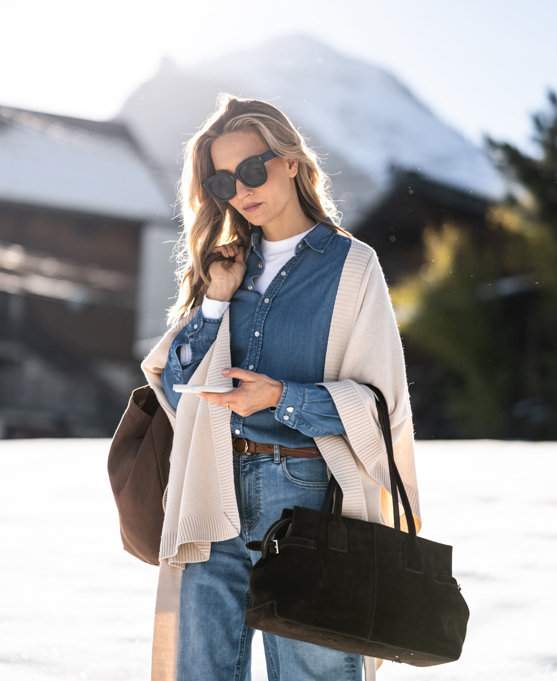 Woman wearing a Tencel denim blouse stands in snow with mountains behind.
