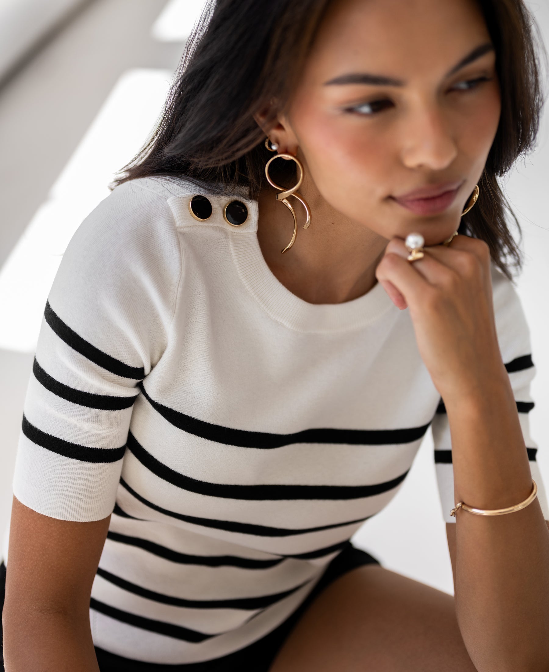 Woman wearing an ivory-black Breton striped sweater, seated and smiling softly.
