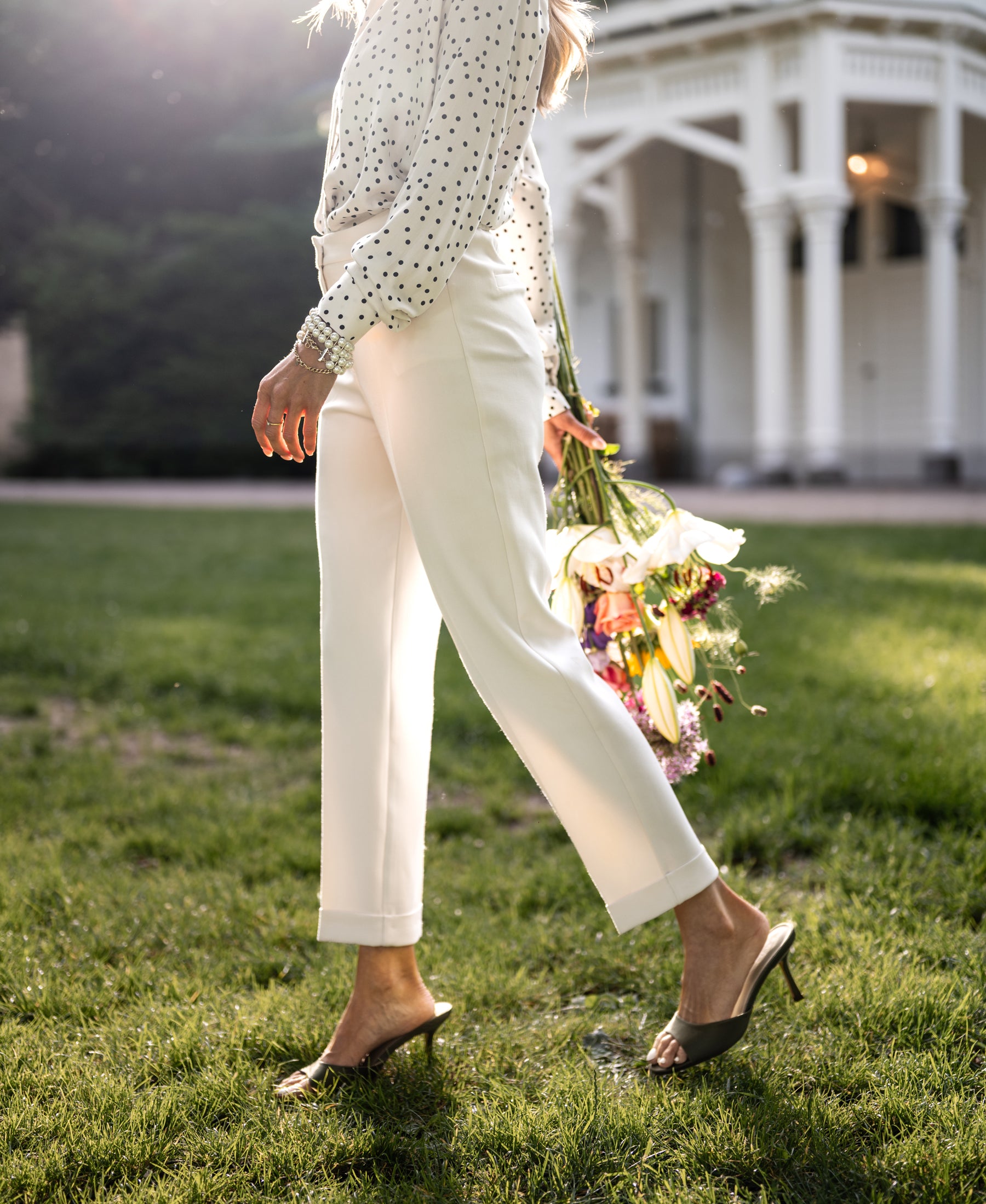 Cream pants in a straight-leg style shown outdoors with sunlight and flowers in the background.