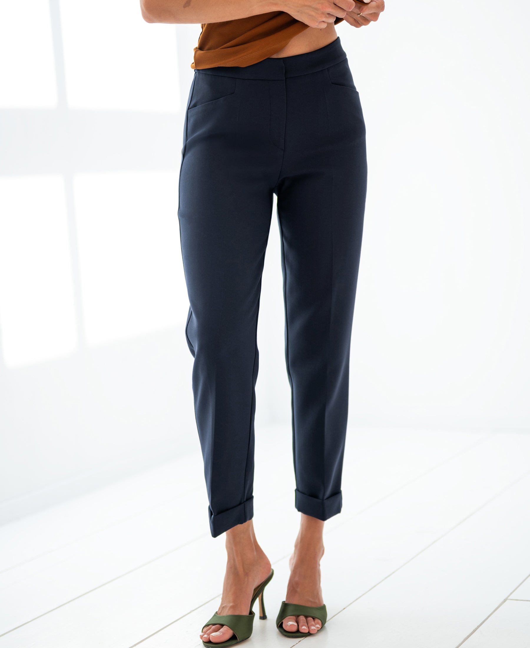 Woman wearing dark blue PLEIN PUBLIQUE 7/8 LE FAUBOURG trousers, standing on a white floor in a bright room.