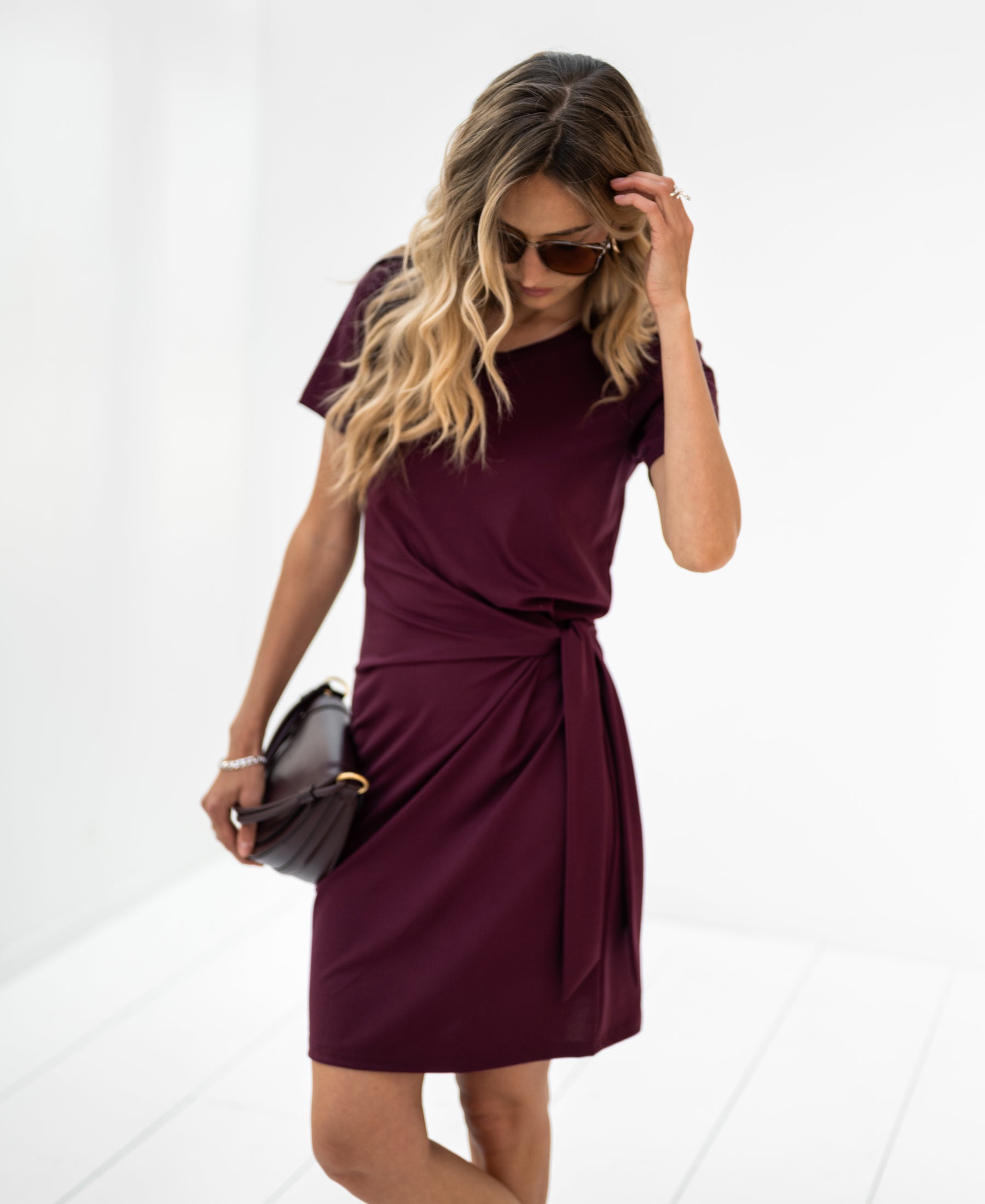 Woman wearing the red LA FEE Button Dress by PLEIN PUBLIQUE stands by a white wall.