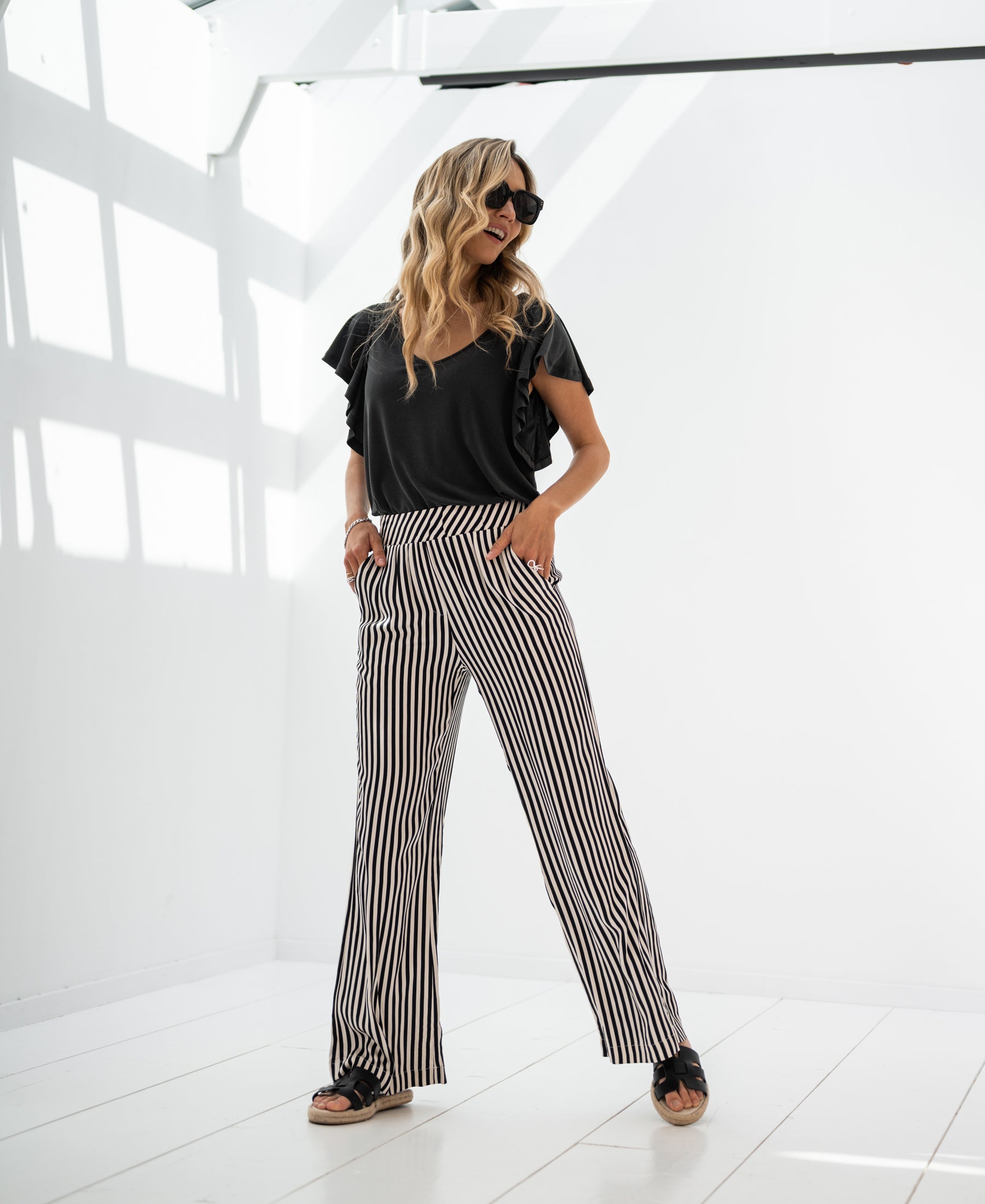 Ivory-black striped LA MONET trousers by PLEIN PUBLIQUE, shown in a bright, minimalist room.