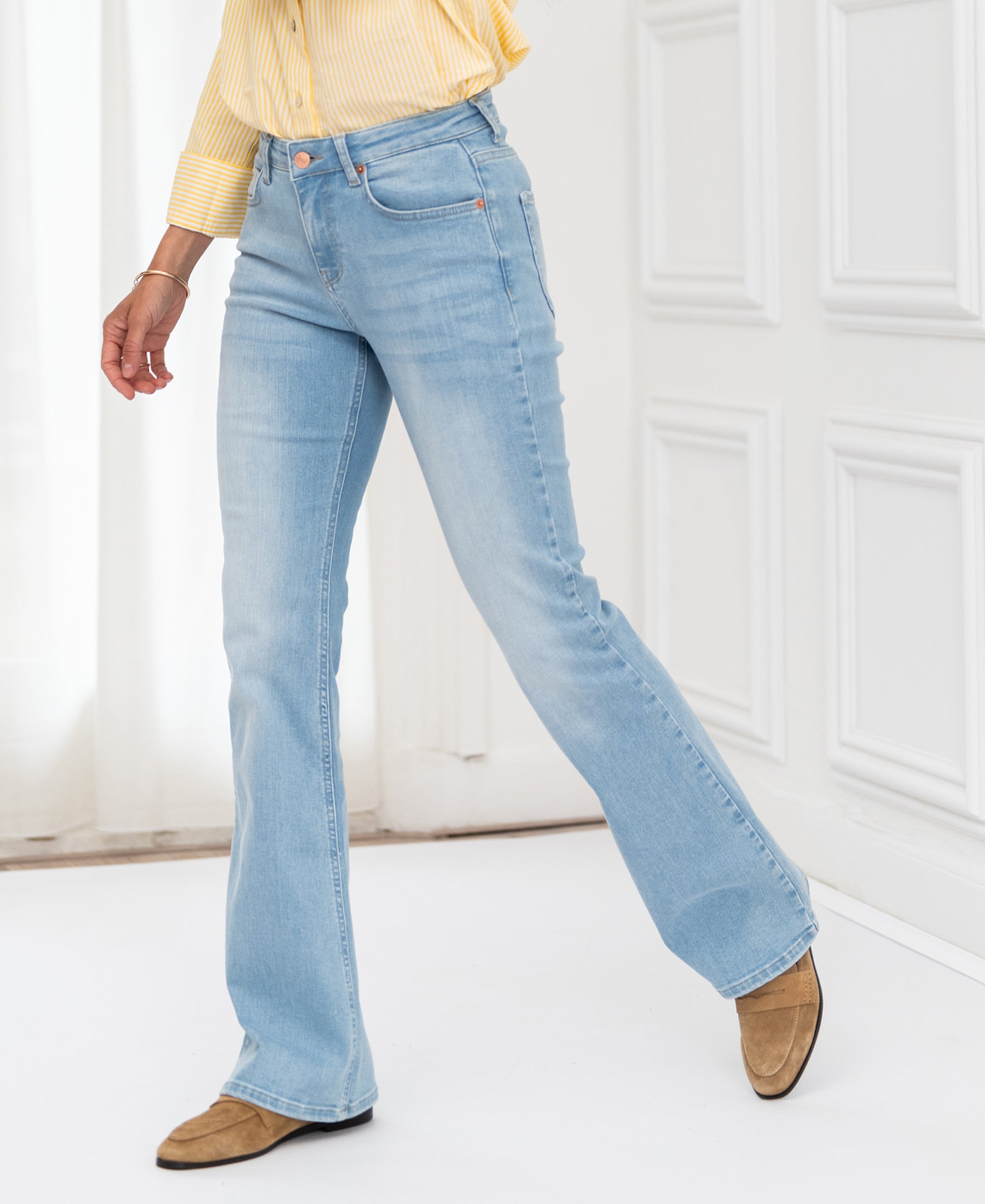 Person wearing bleached flare jeans near white-paneled walls.