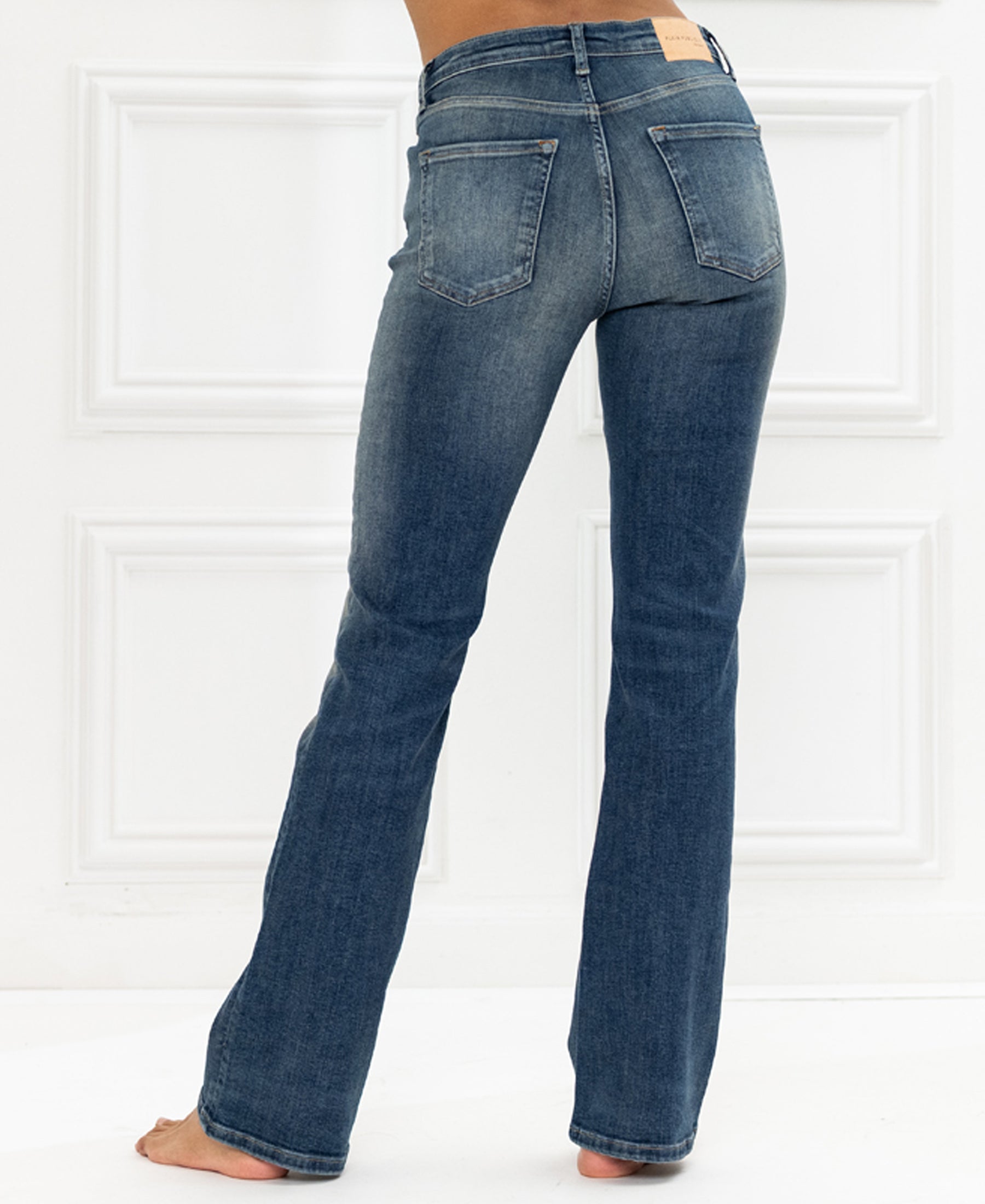 Blue vintage flared jeans, back view, shown against a white paneled wall.