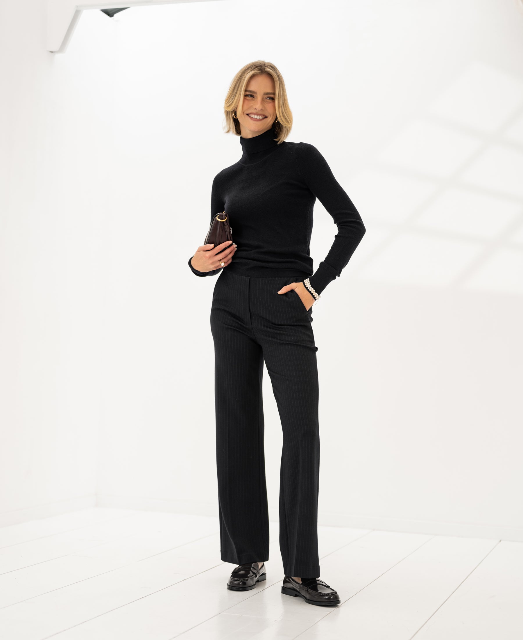 Black Merino wool turtleneck sweater by PLEIN PUBLIQUE displayed in a bright, minimalist room.