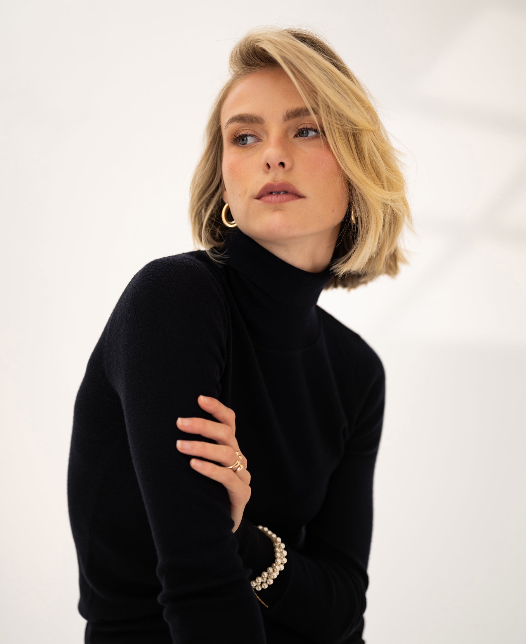 Woman wearing a black merino wool turtleneck sweater, looking aside.