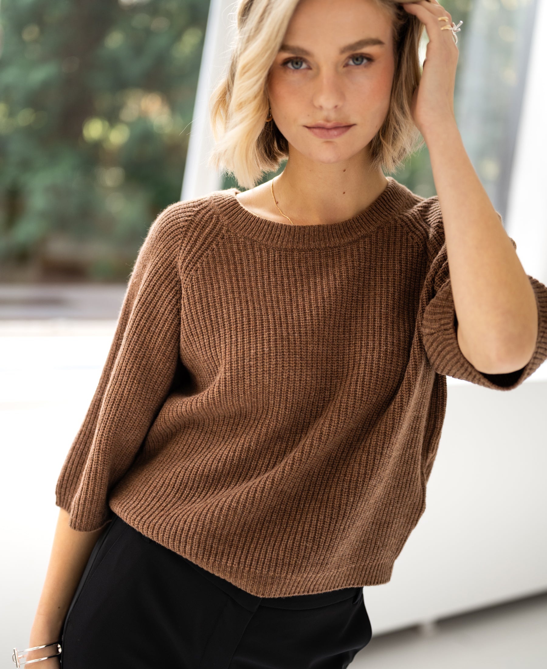 Model wears the PLEIN PUBLIQUE LA FRAMBOISE tobacco-colored sweater indoors.